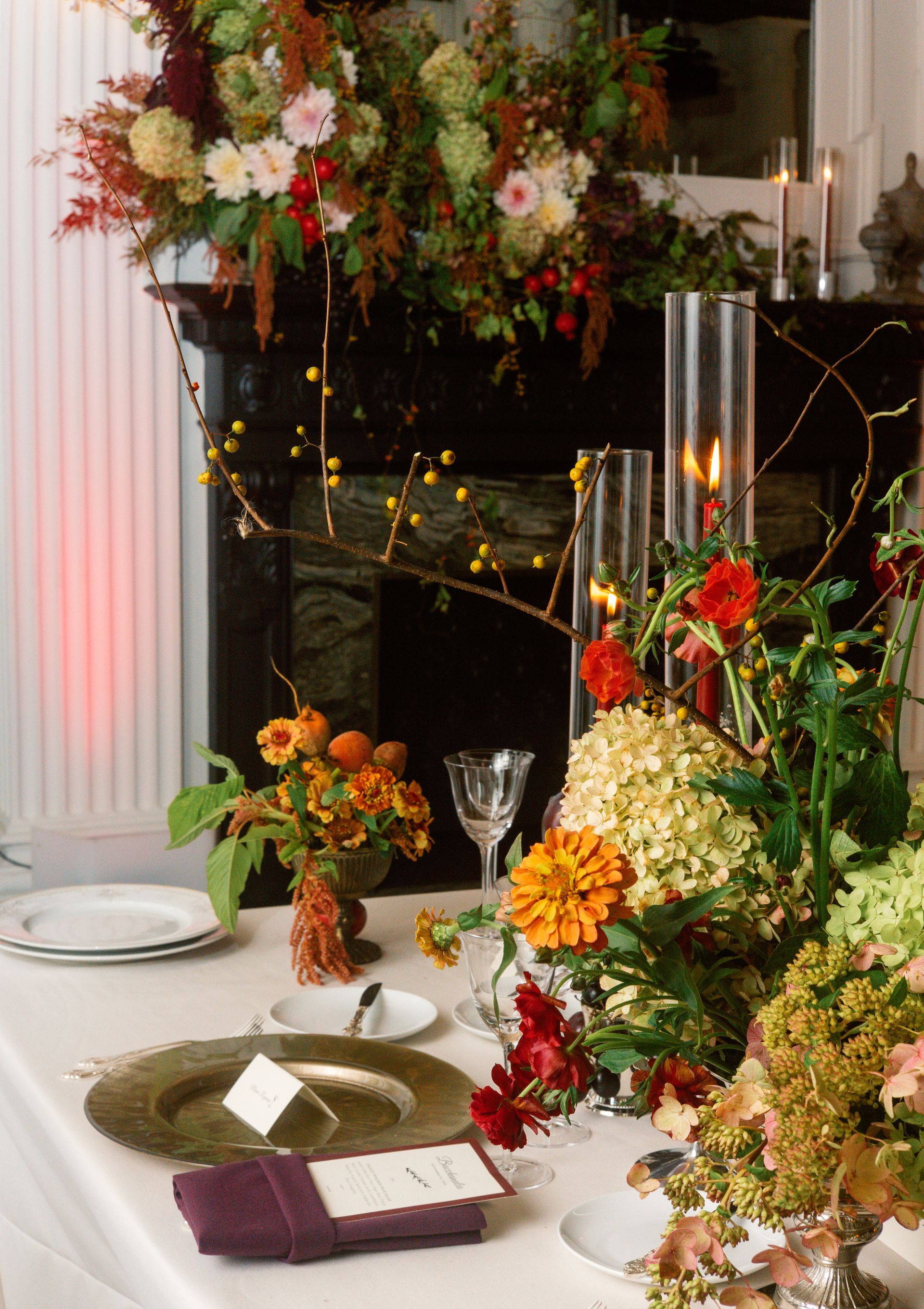 Elegant table setting with colorful floral arrangements, candles, and glassware beside a decorated fireplace