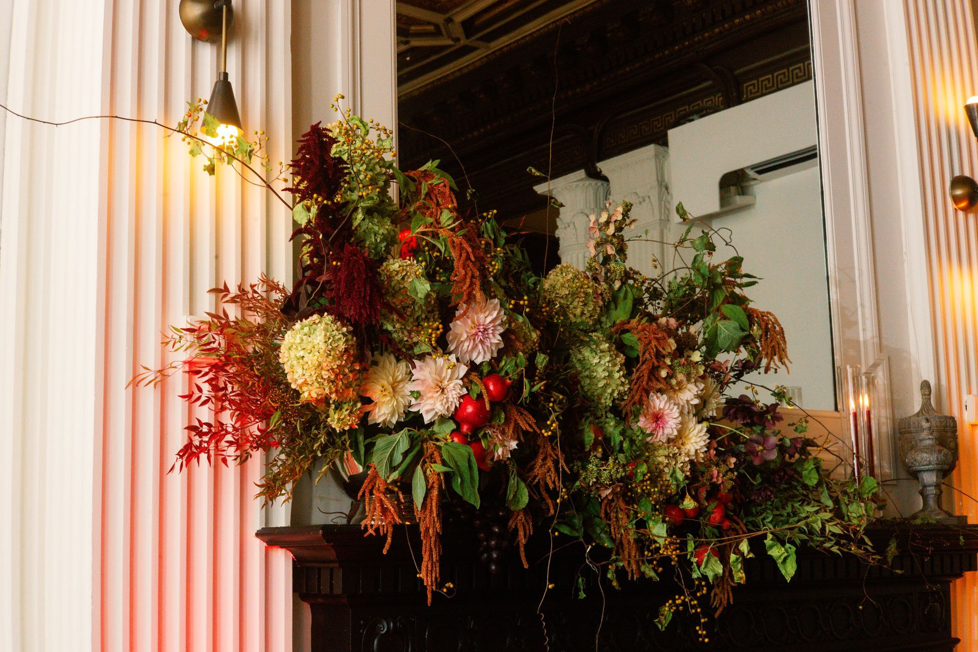 Floral arrangement with red, orange, and white flowers on a mantel beside white columns