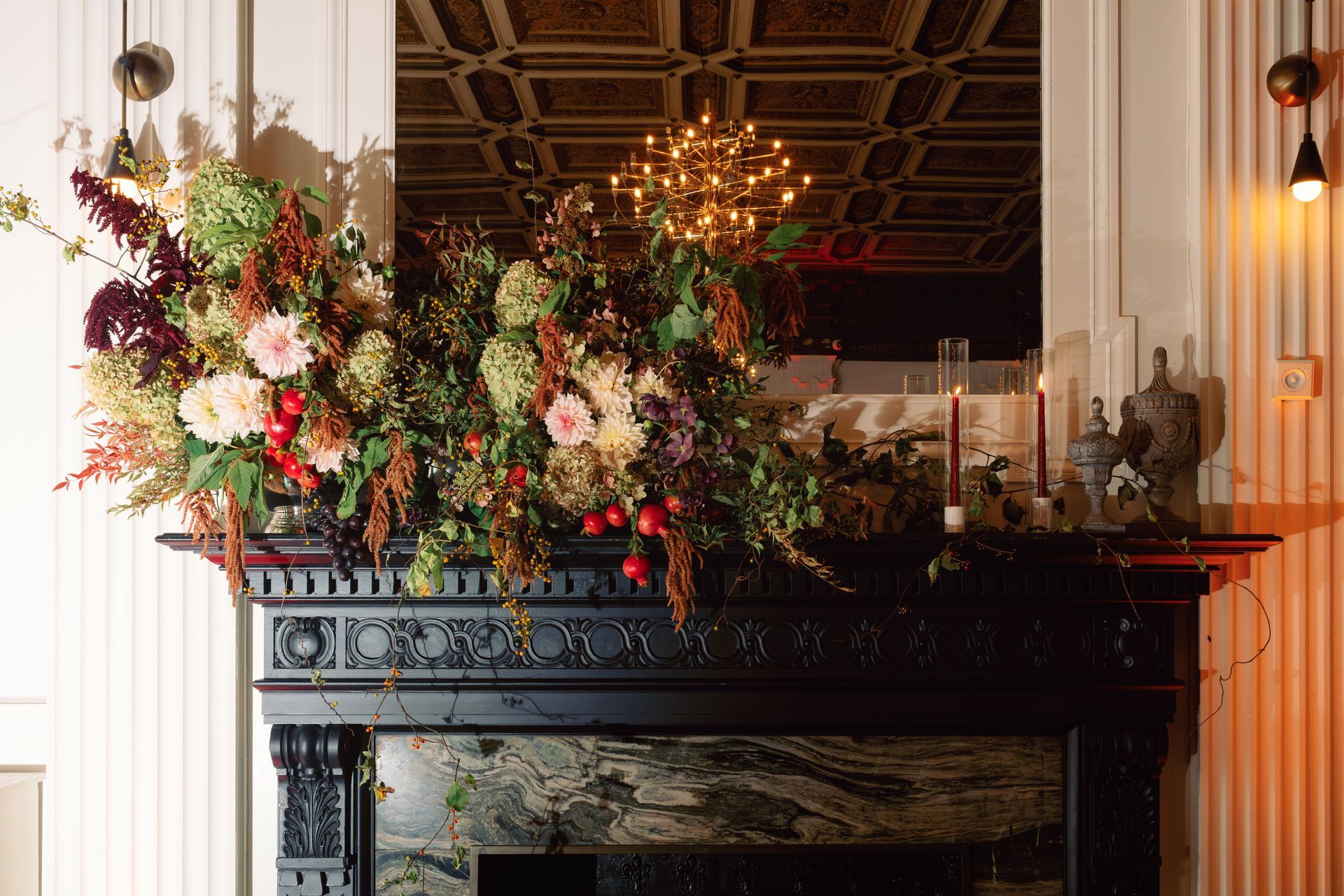 Floral arrangement with pink and white flowers on a black fireplace mantel in an ornate room