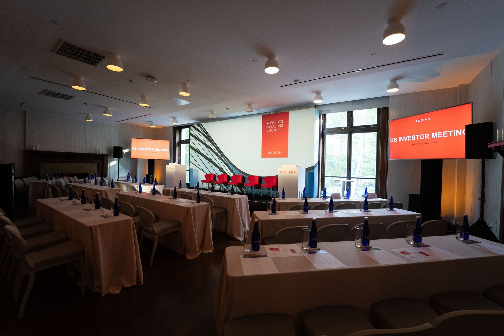 Conference room with rows of tables, orange presentation screens, and a staircase in the back.