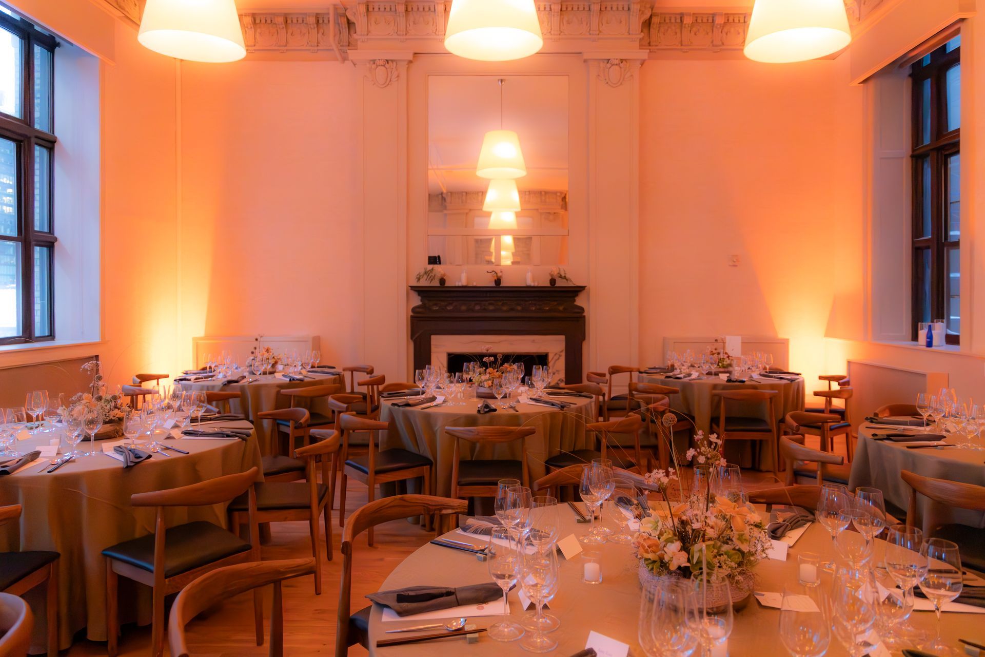 Elegant dining room with round tables set for a formal event, warm orange lighting, and a fireplace at the far end