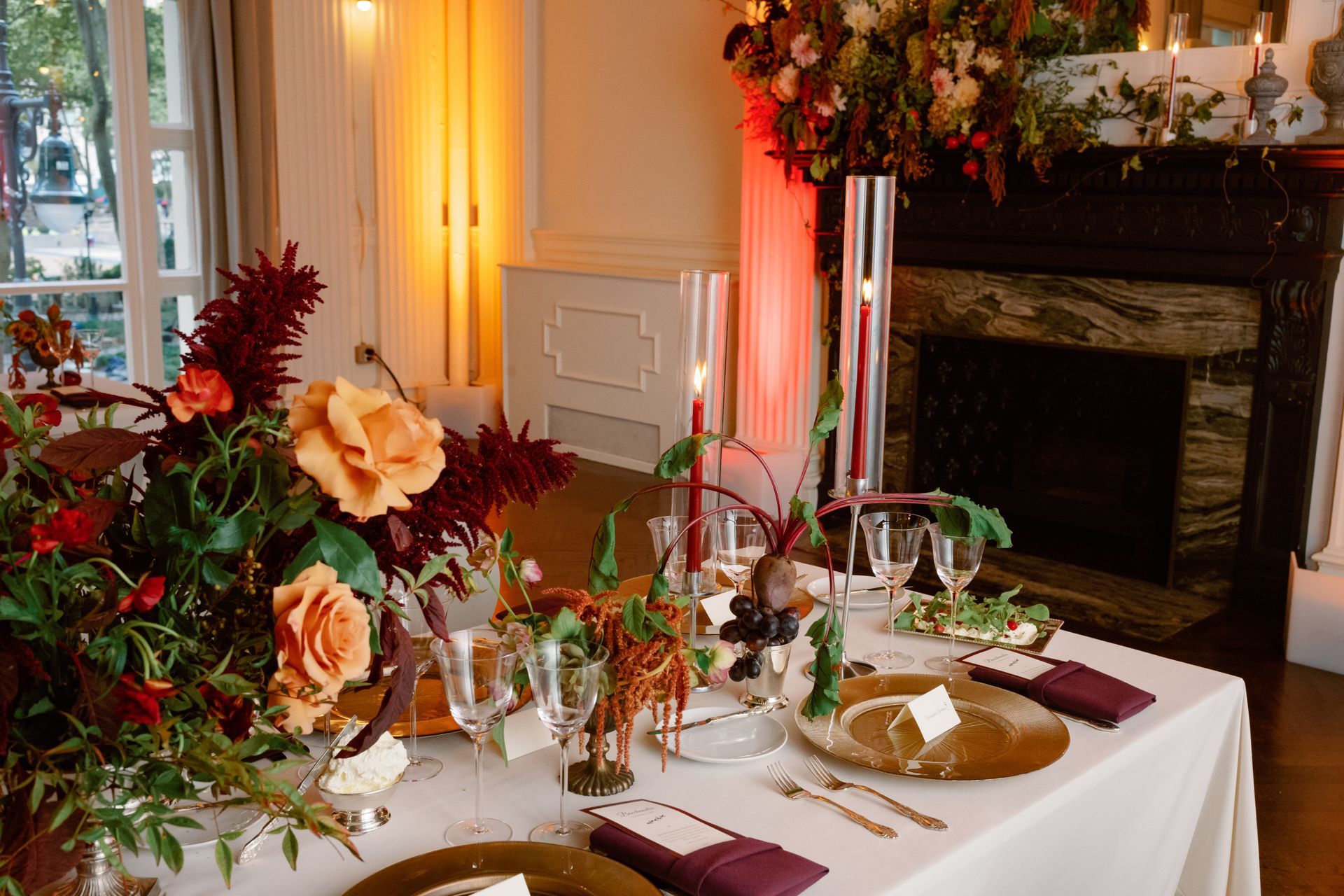 Elegant dining table set with flowers and candles beside a fireplace in a warmly lit room