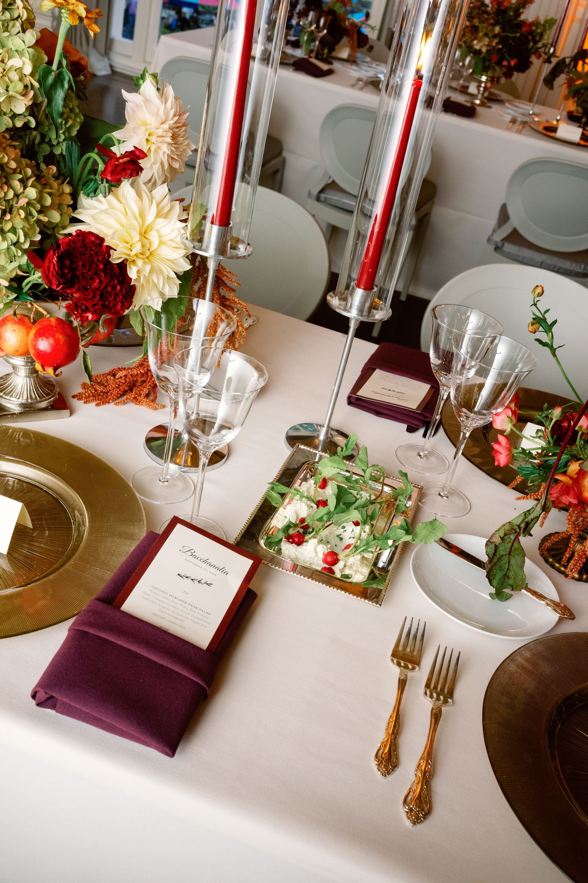 Decorated dining table with gold plates, red flowers, candles, and burgundy place cards at a formal event