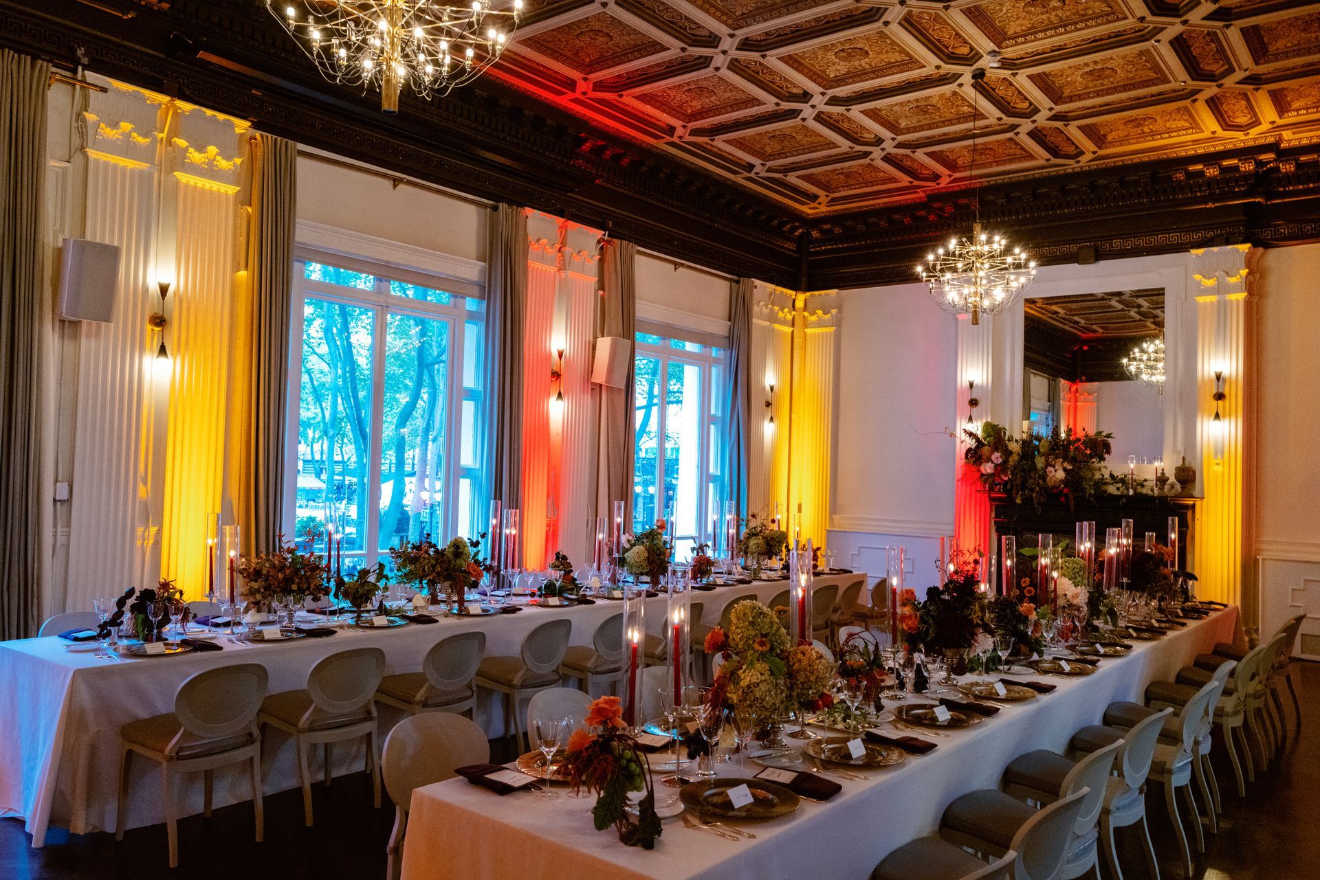 Elegant banquet hall with long candlelit tables, white chairs, chandeliers, and blue-lit windows