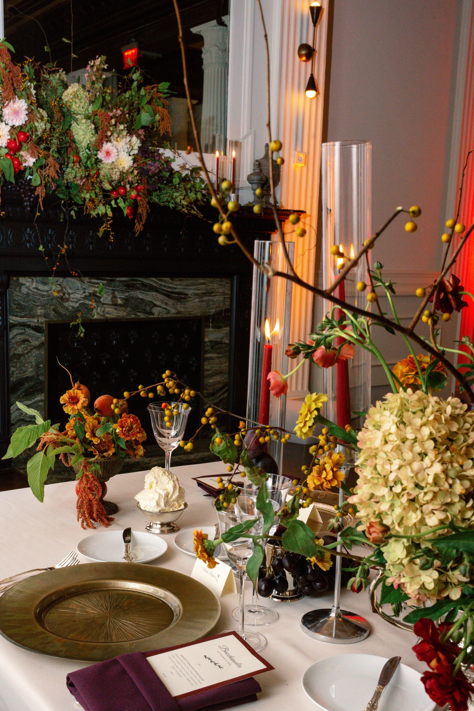 Flower-filled table setting with plates, candles, and a green dish in a softly lit room