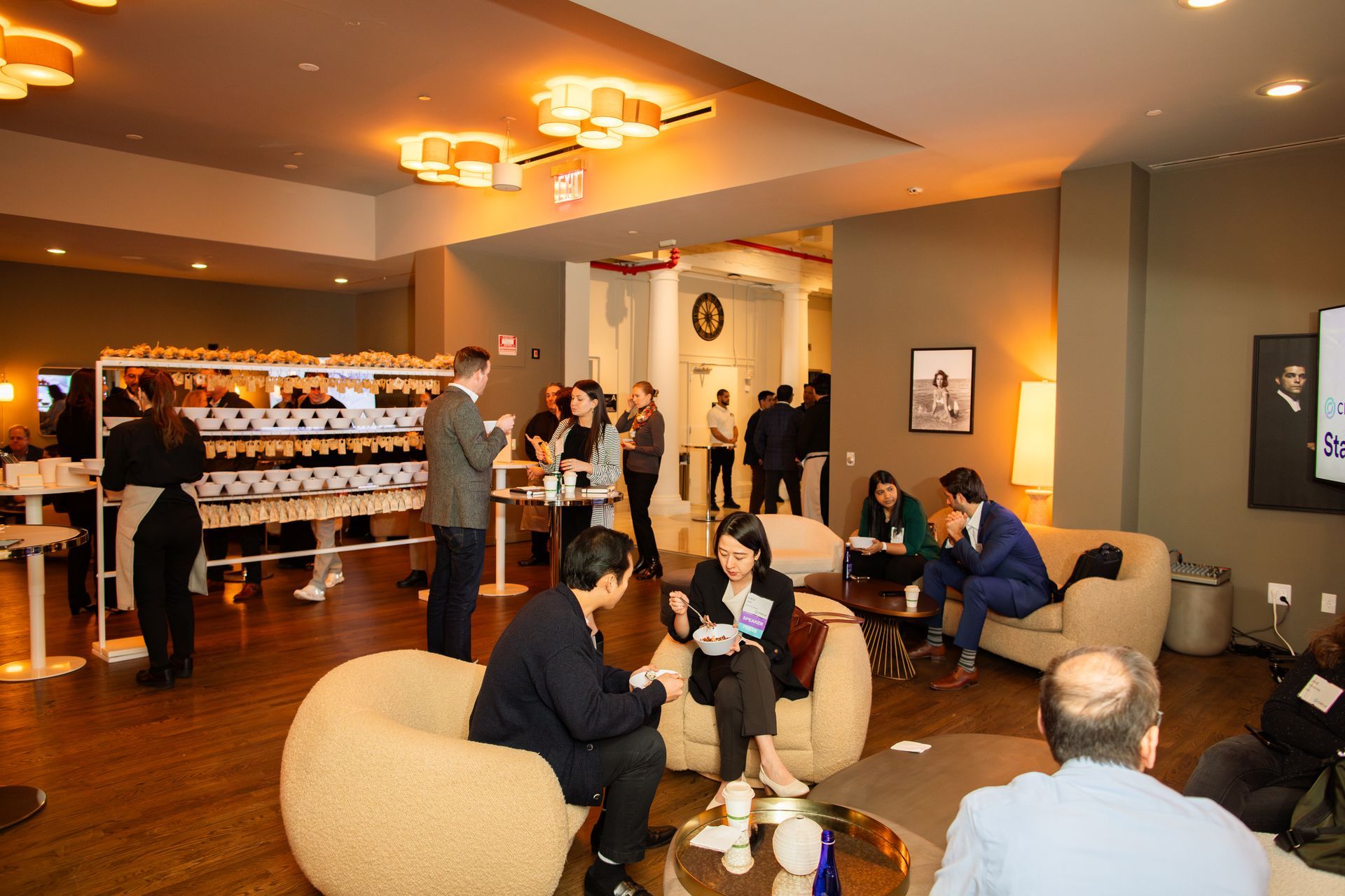 People chatting in a warmly lit lounge with sofas, tables, and a bar area