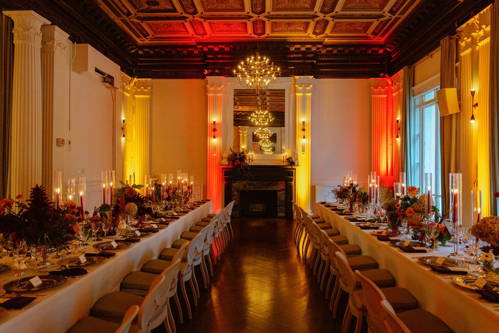 Elegant banquet hall with long candlelit table, chandeliers, and warm red-orange lighting