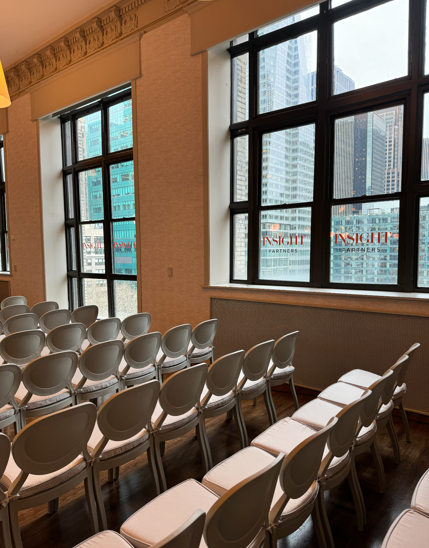 Empty classroom with rows of white chairs by large windows in warm sunlight