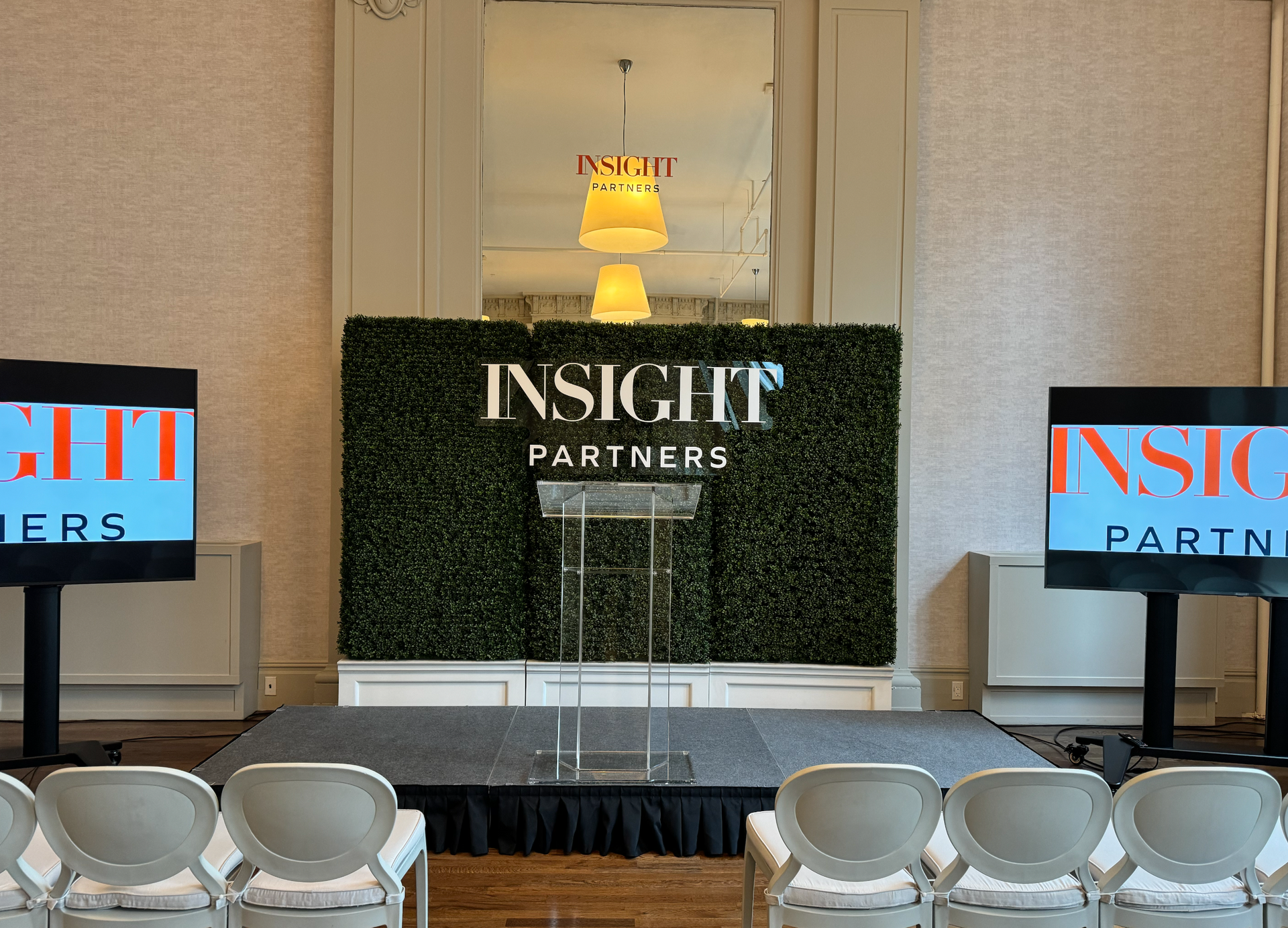 Conference stage with INSIGHT Partners backdrop, two side screens, and white chairs in front.