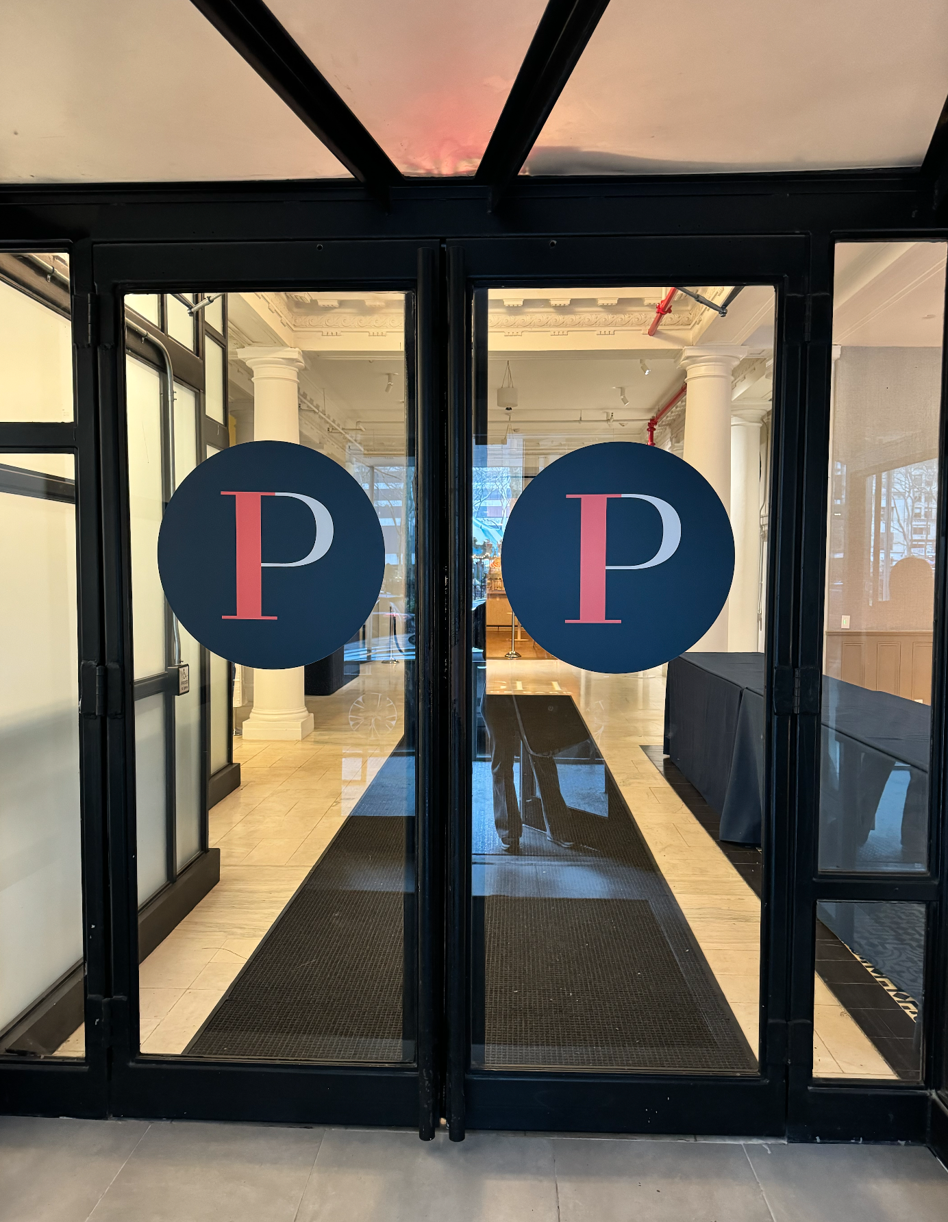 Glass entrance doors with blue “P” signs and a hallway visible inside