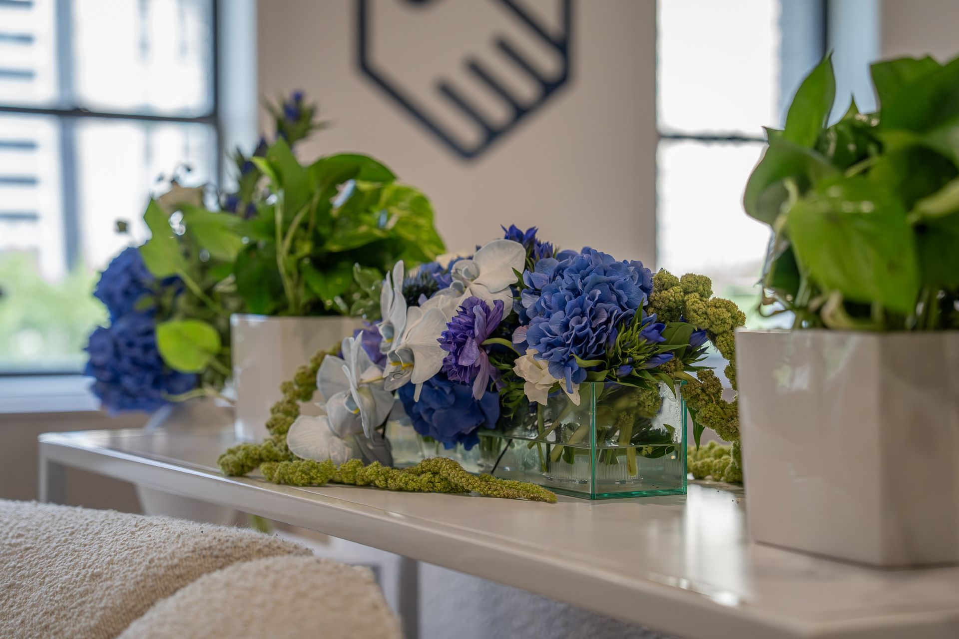 Bouquets of white and blue flowers on a table in a bright indoor room with potted plants