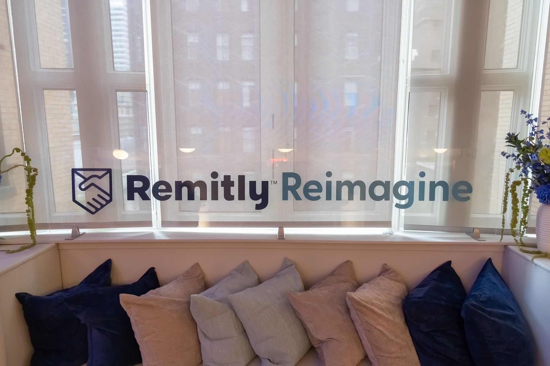 Remitly Reimagine logo on a window above a couch with blue and beige pillows