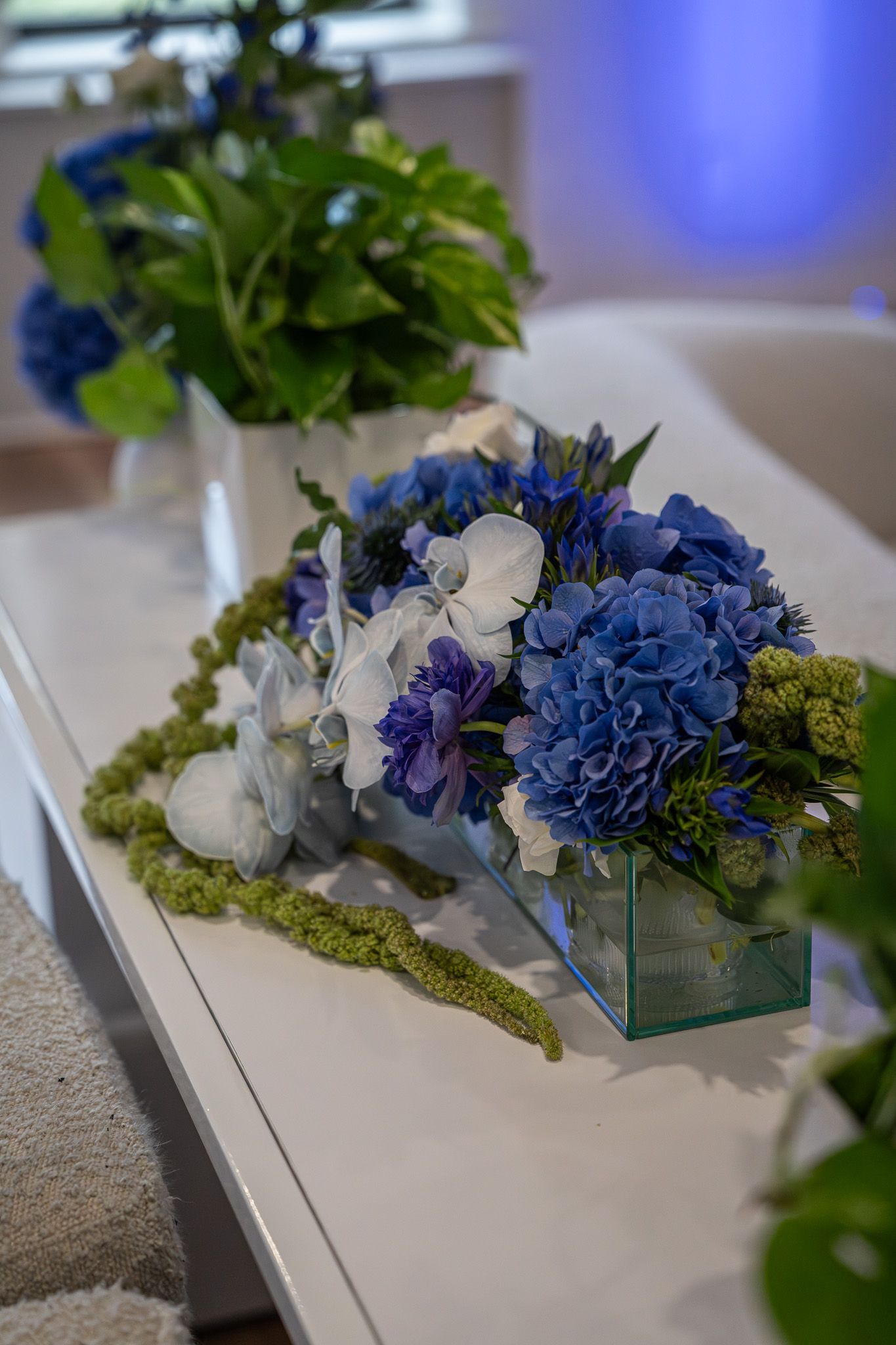 Blue and white floral centerpiece on a long table with green foliage accents