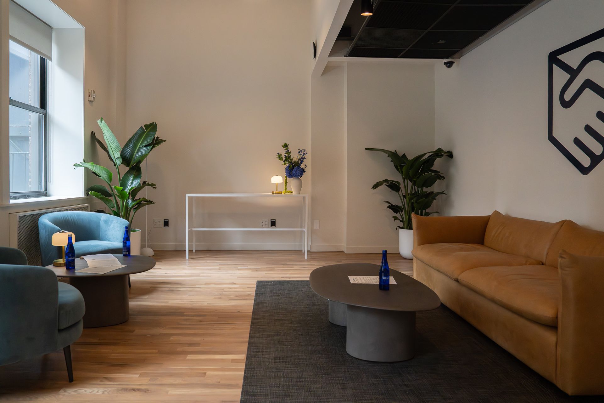 Modern living room with tan sofa, blue chair, coffee table, plants, and wood floor