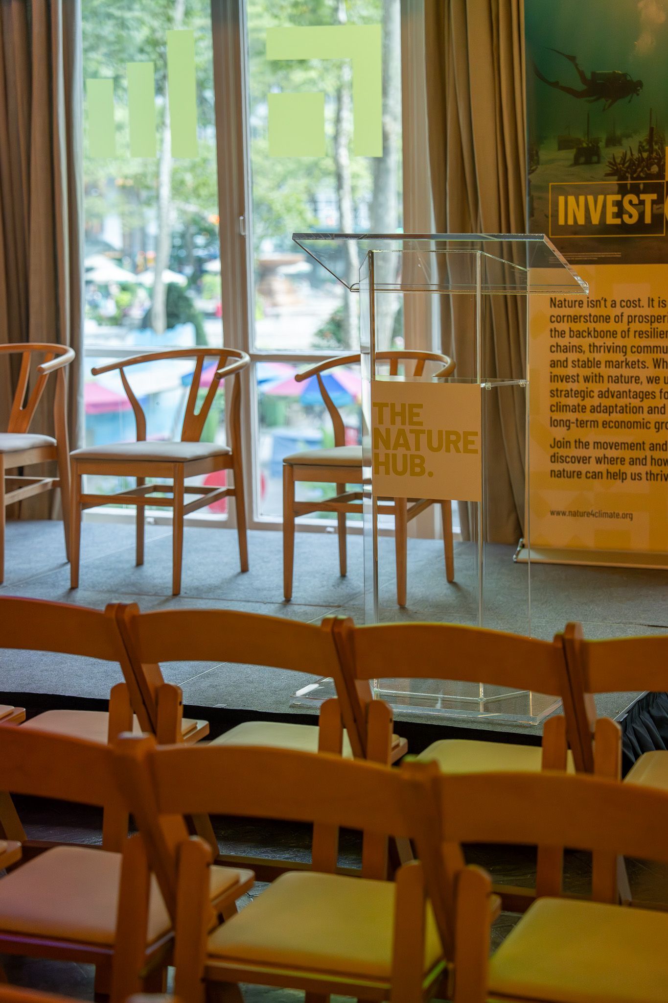 Empty café seating area with wooden chairs and a clear podium near a large window.