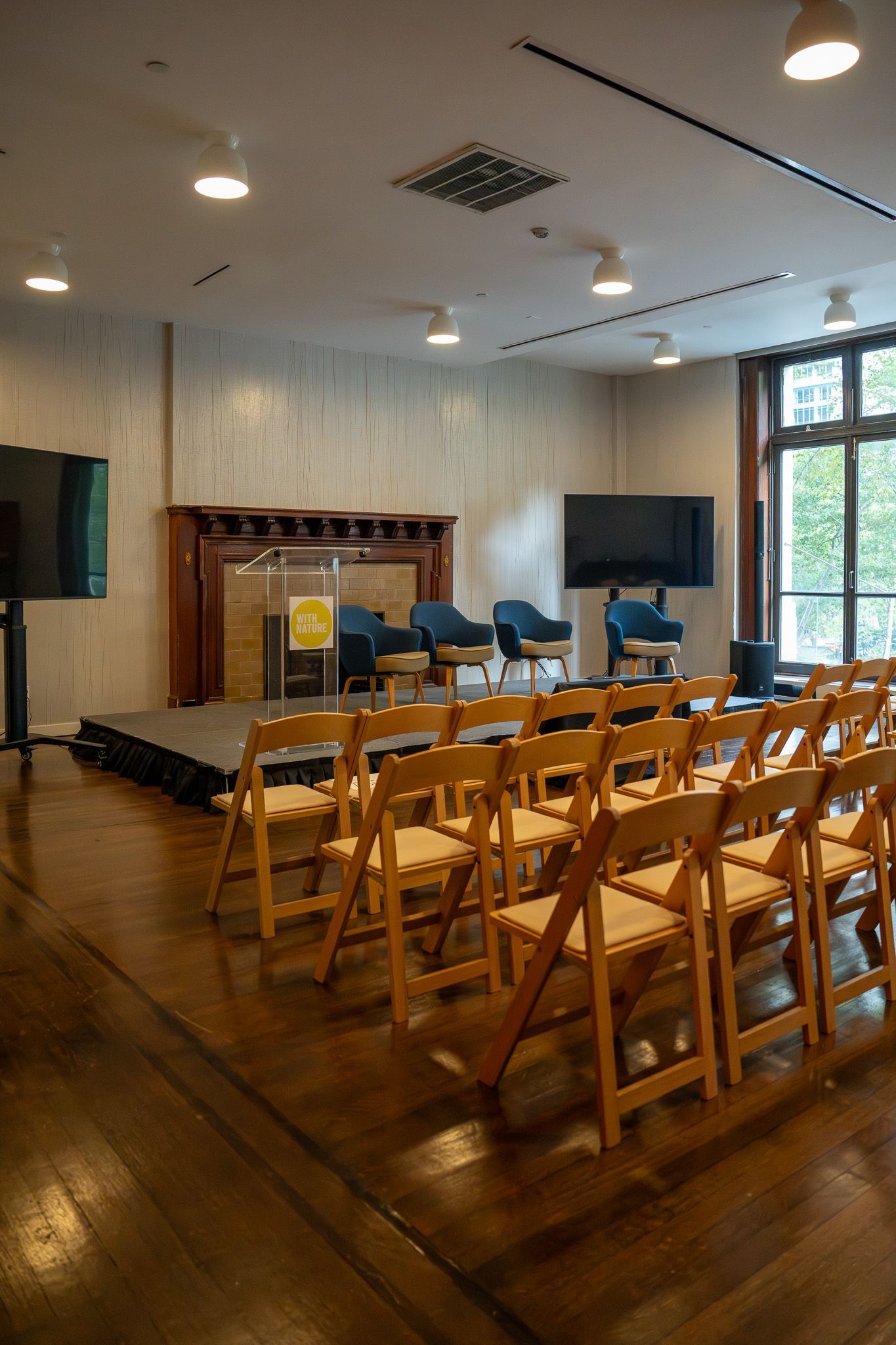 Conference room with rows of wooden chairs facing a stage and presentation screen