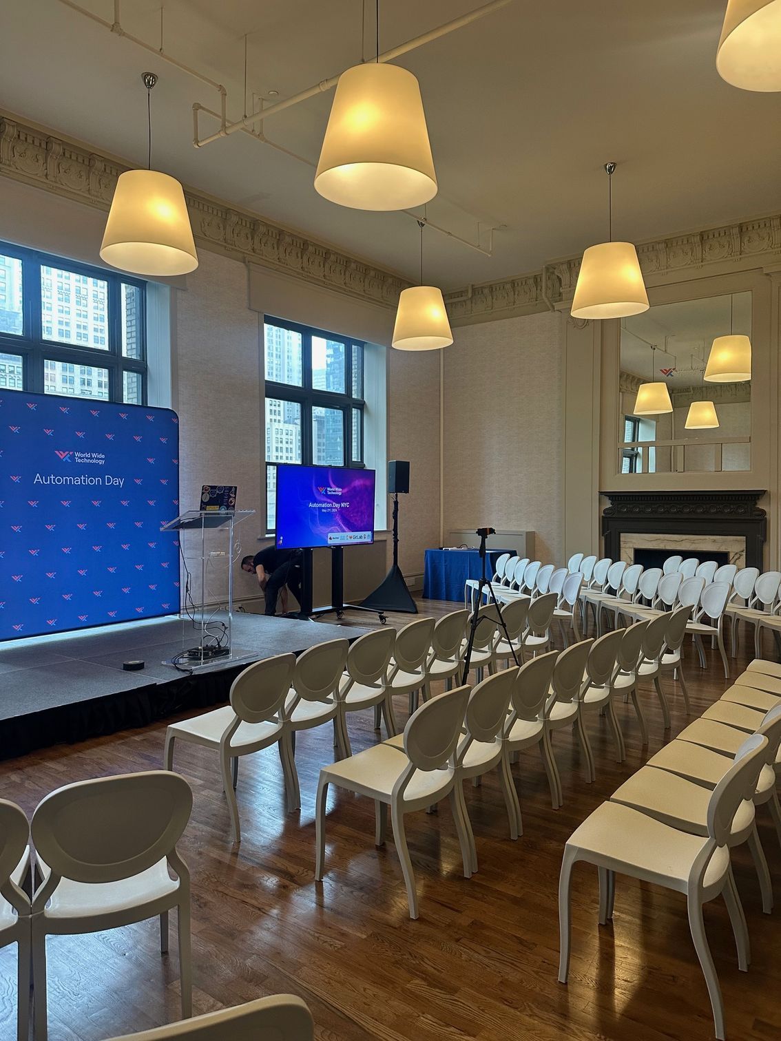 Conference room with rows of white chairs, a stage screen, and hanging pendant lights.