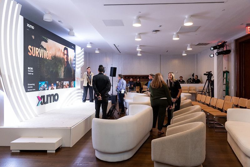 People gathered in a modern event space with a large presentation screen and white lounge seating.