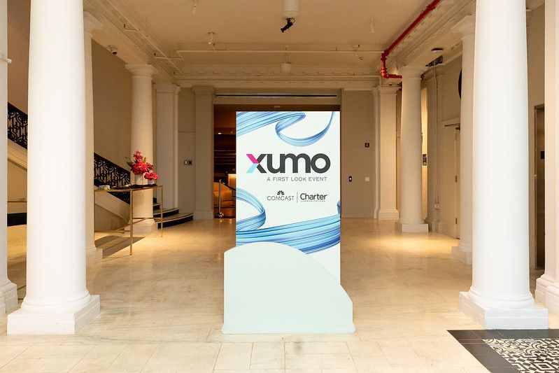 Xumo sign on a stand in a bright, white-columned lobby