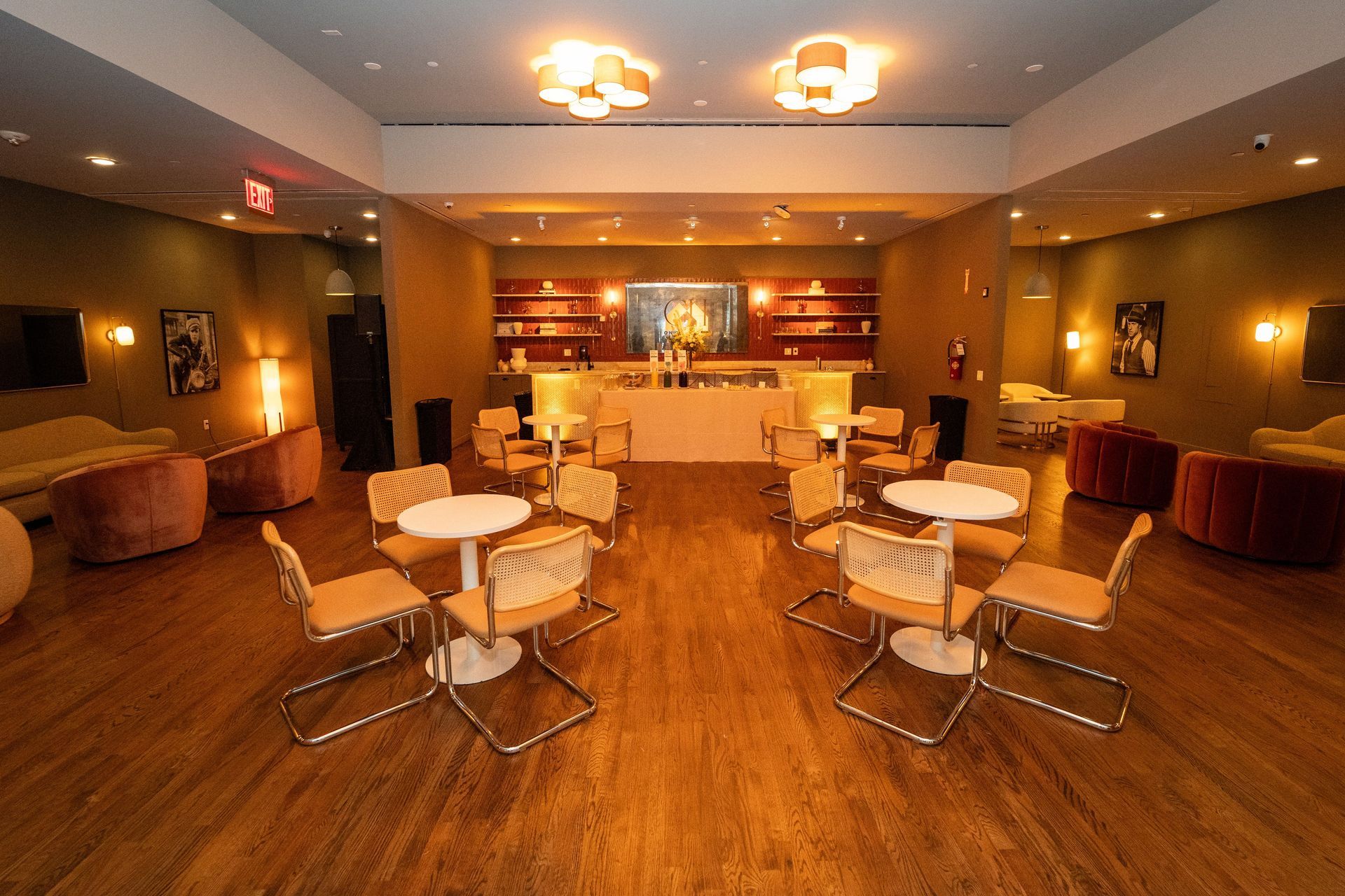 Warmly lit lounge with round tables, chairs, and a bar in the background