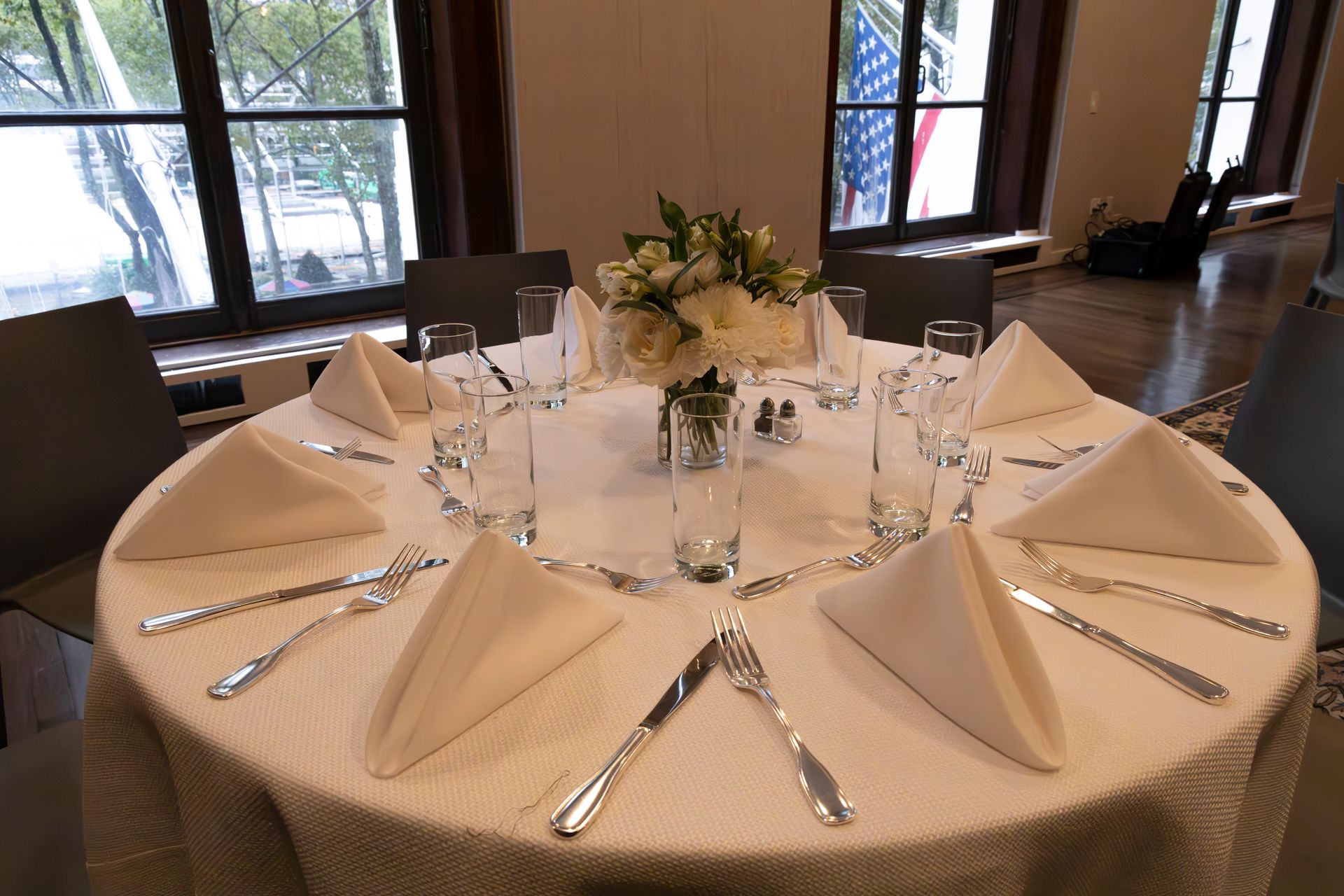 Set dining table with folded napkins, glassware, and a floral centerpiece in a banquet room