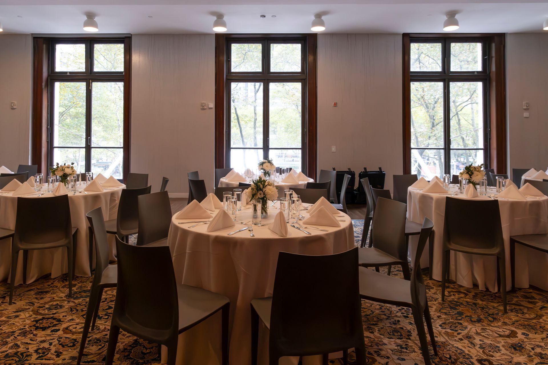 Elegant banquet hall with round tables, beige tablecloths, and tall windows letting in soft daylight