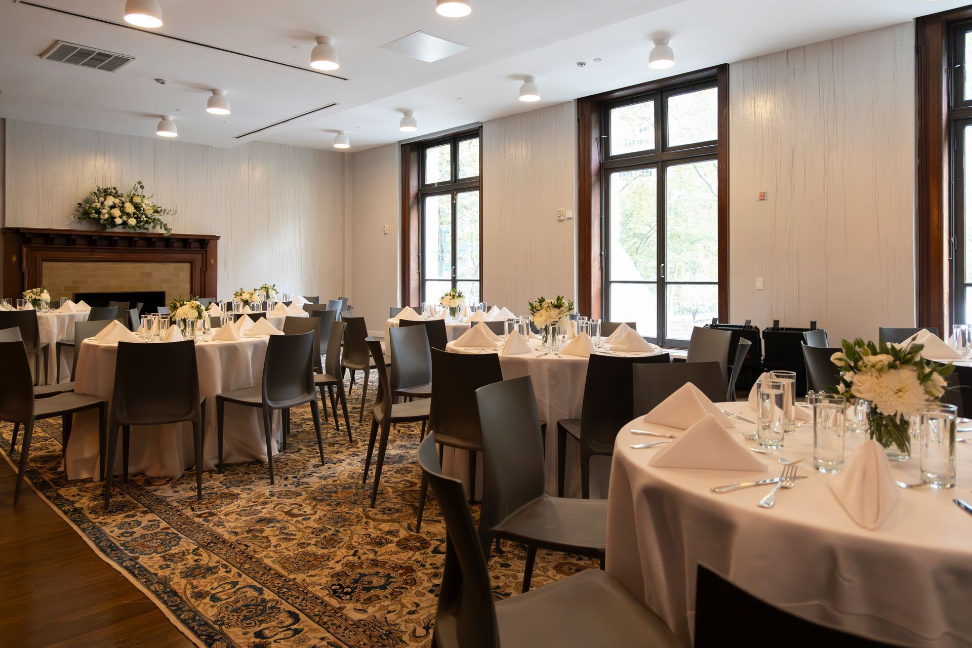 Elegant banquet room with round tables set for a formal event and tall windows along the wall