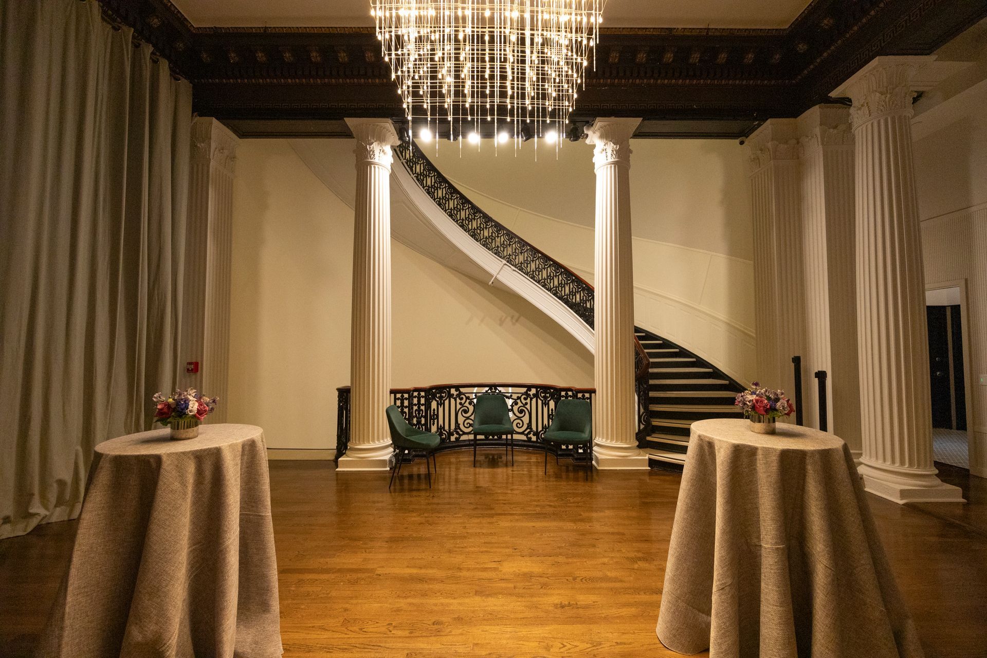 Elegant ballroom with a grand staircase, chandelier, and two cocktail tables on a polished wooden floor