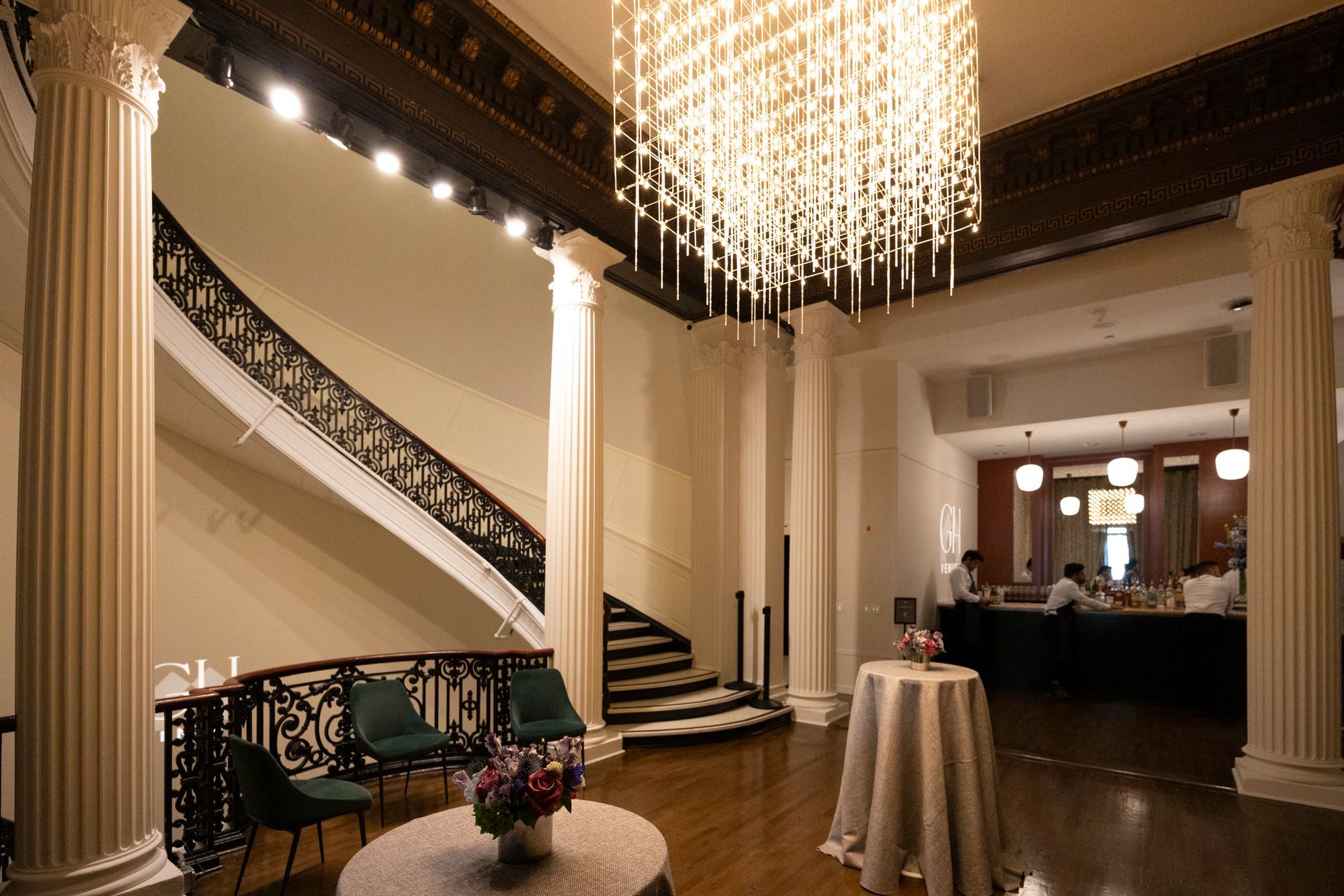 Elegant lobby with chandelier, curved staircase, and cocktail tables in a warmly lit hall