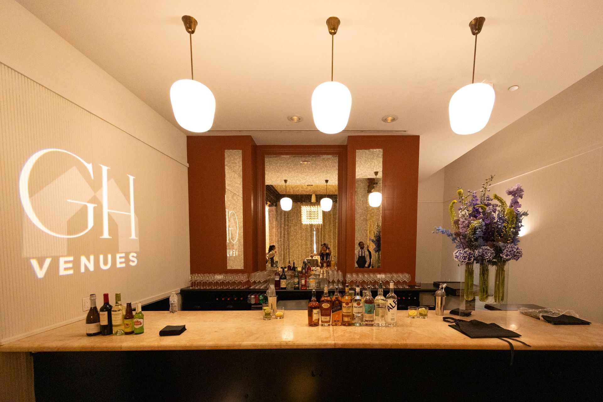 Elegant hotel bar with warm lighting, bottles on the counter, and white pendant lamps above the mirror-back wall