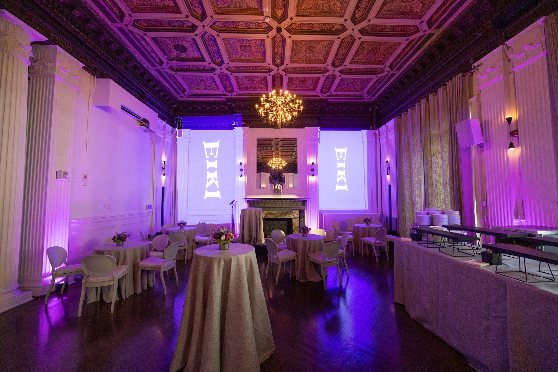 Elegant banquet hall with purple lighting, chandeliers, and set tables for an event