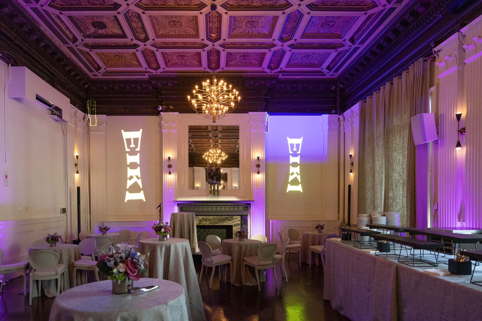 Elegant banquet room with purple lighting, round tables, chandeliers, and buffet setup