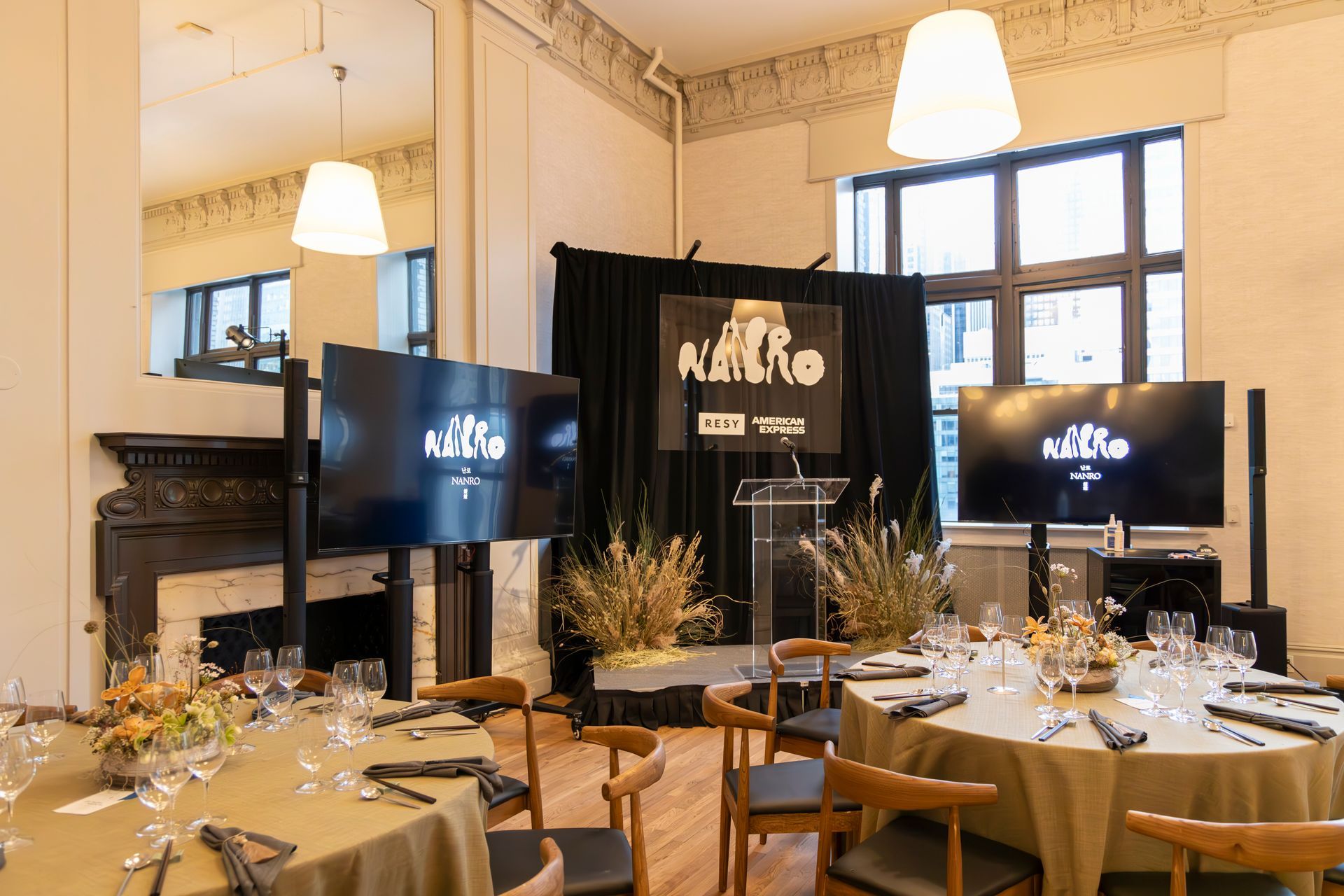 Event dining room with set tables, black stage screens, and warm pendant lights