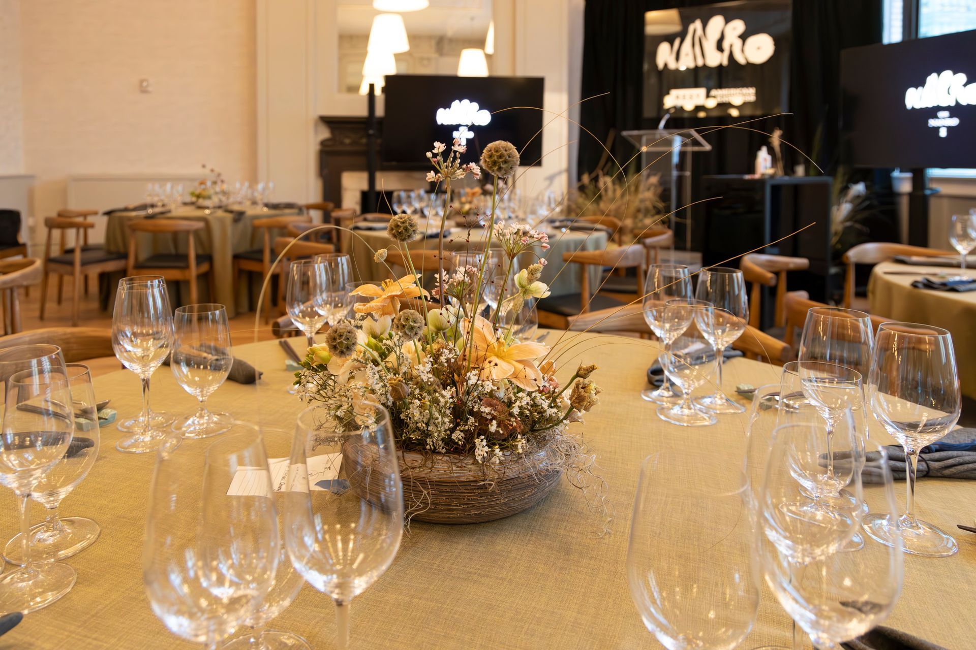 Elegant dining table set with wine glasses and a floral centerpiece in a warmly lit event hall