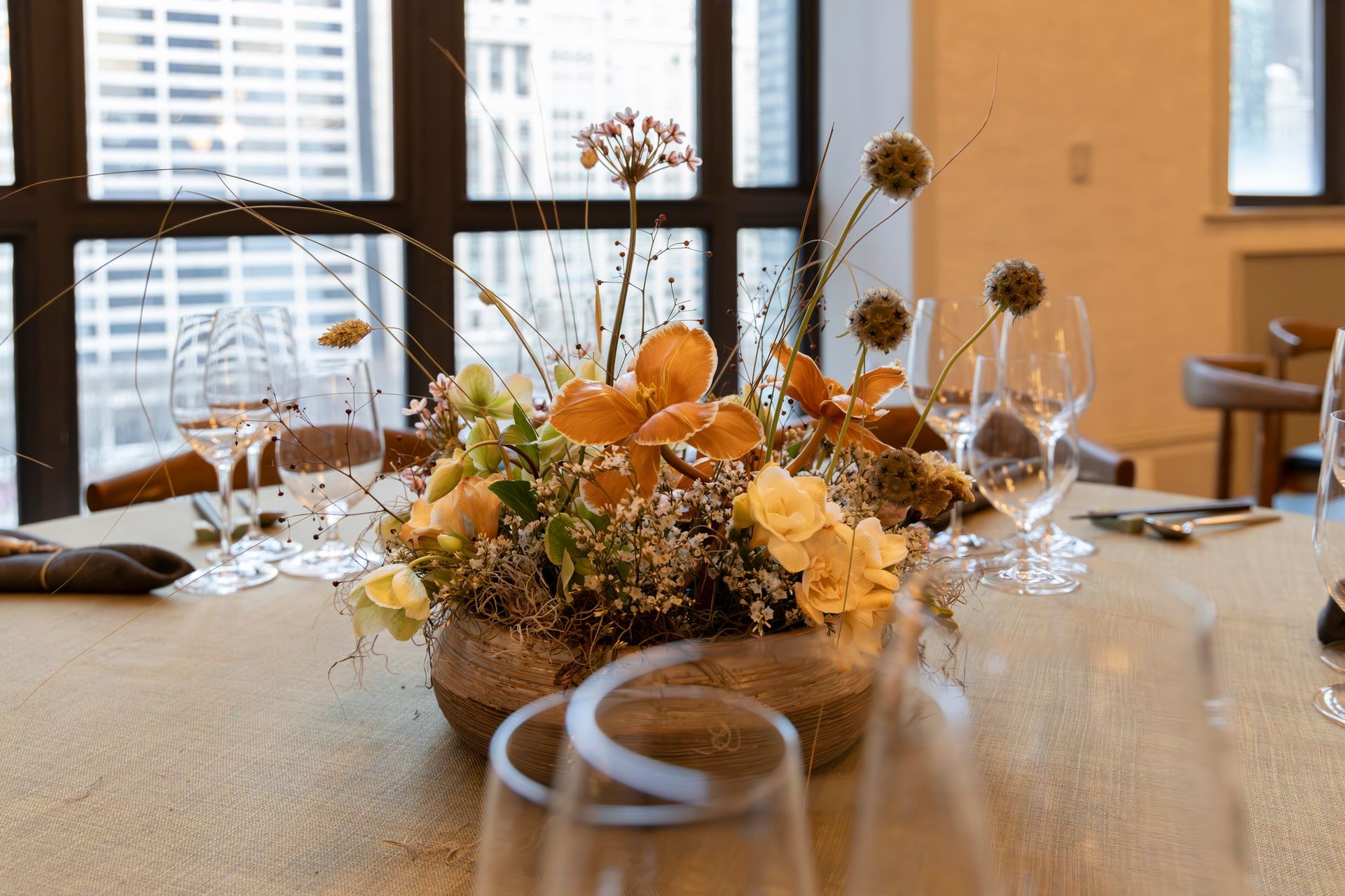 Elegant dining table with a floral centerpiece, glassware, and city-view windows in the background