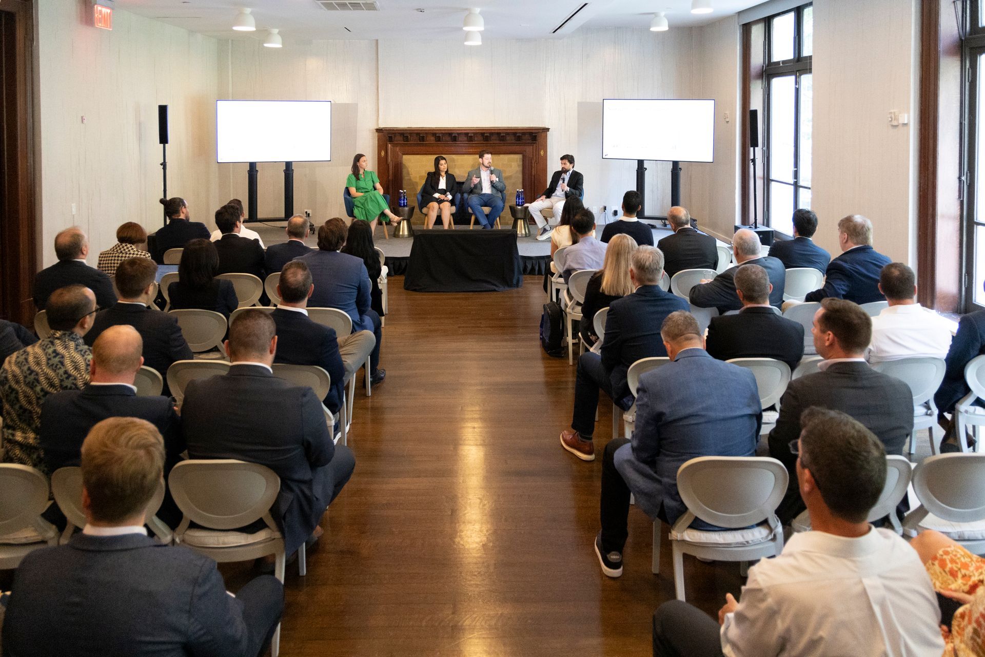 Conference room with an audience seated facing a panel at the front, with projection screens on both sides.