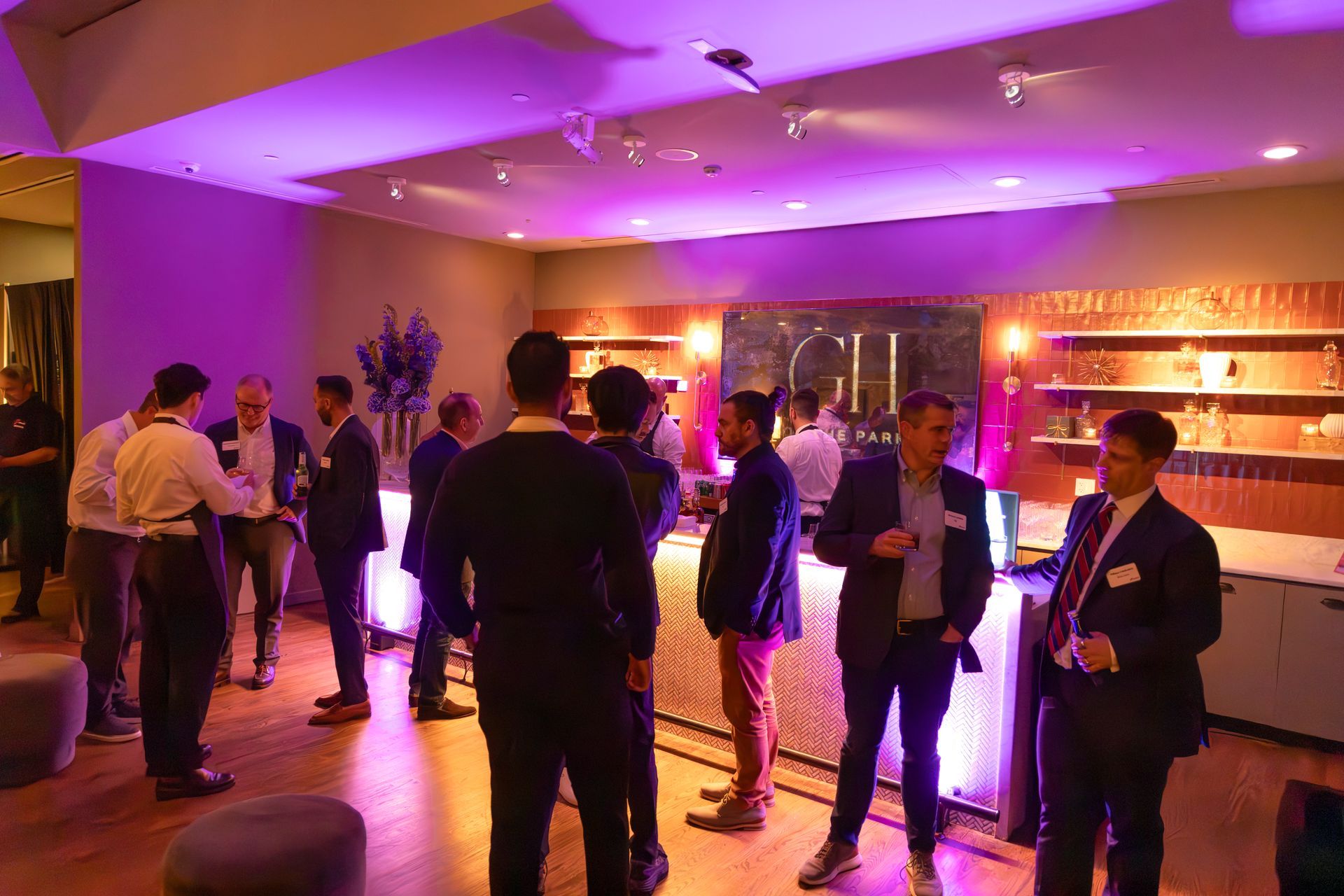 People mingling at a dimly lit indoor event with purple lighting and glowing tables