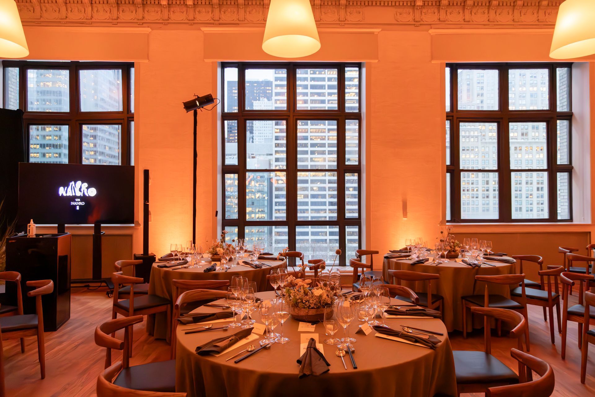 Orange-lit restaurant dining room with set tables, chairs, and large windows in the background