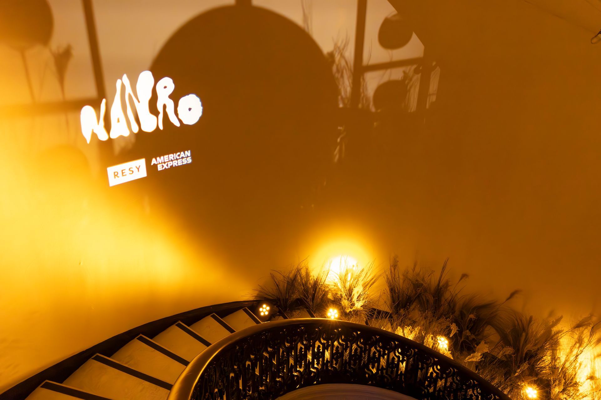Orange-lit Nairo venue sign above a curved walkway with bright lights and plants