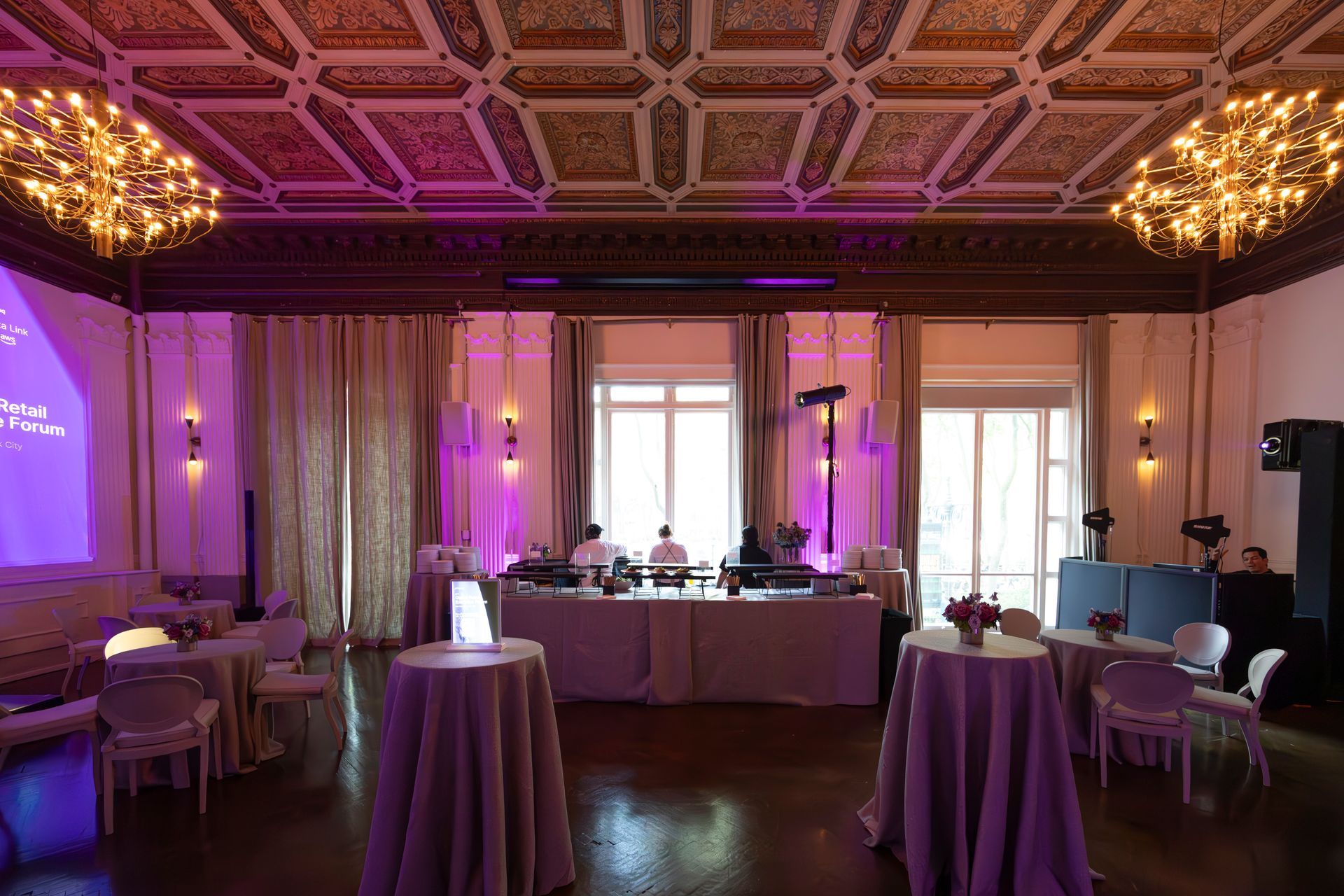 Elegant banquet hall with purple uplighting, round tables, and a decorated ceiling chandelier and stage area