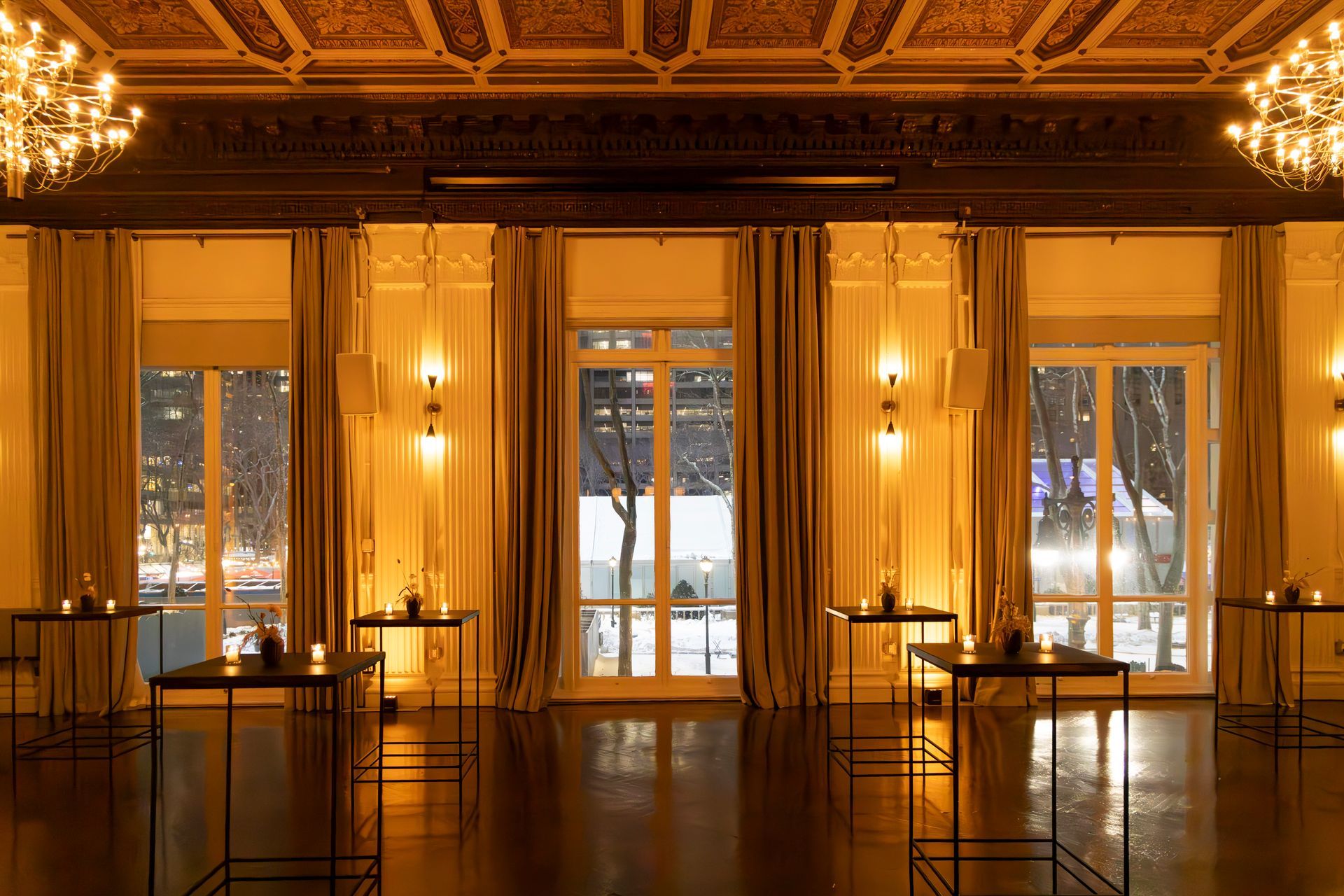 Elegant hall with golden curtains, chandeliers, and large windows overlooking snowy city lights at night