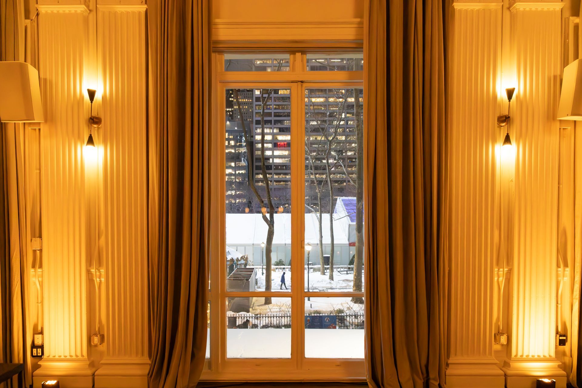 Elegant hallway with tall gold curtains framing a glass door and snowy city view beyond