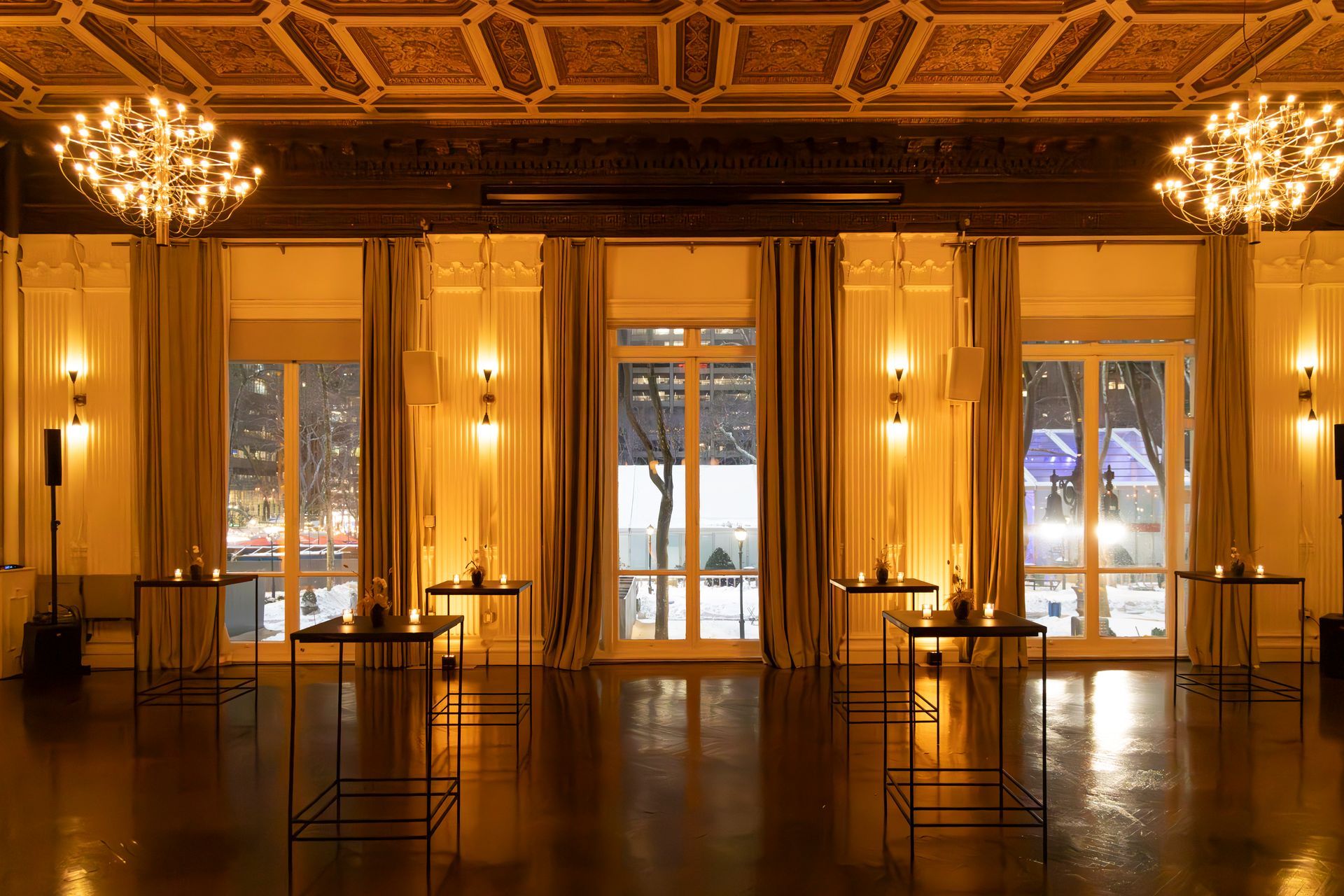 Elegant empty hall with chandeliers, warm wood paneling, and tall windows overlooking snow outside