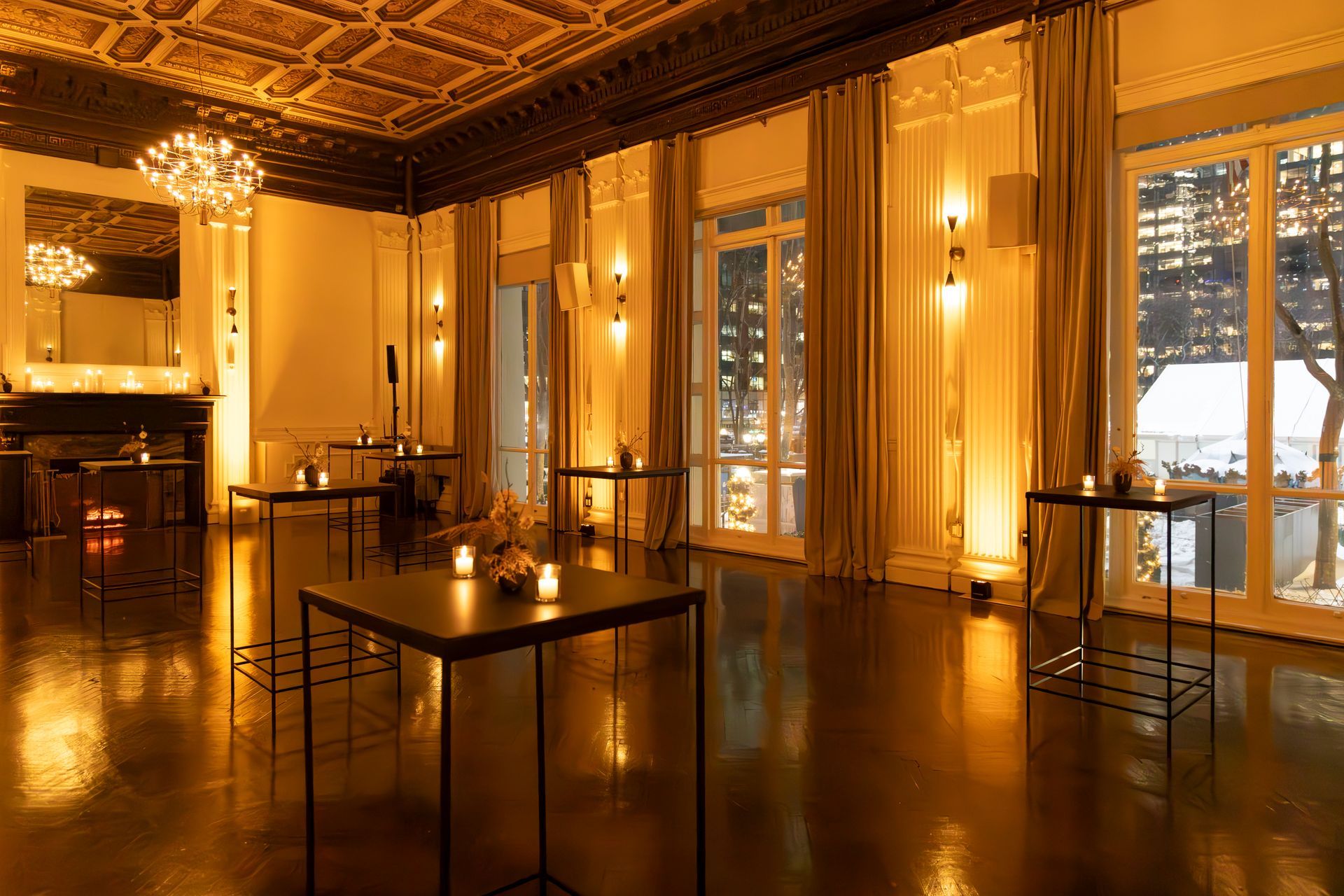 Elegant empty ballroom with golden lighting, tall windows, patterned ceiling, and a few candlelit tables