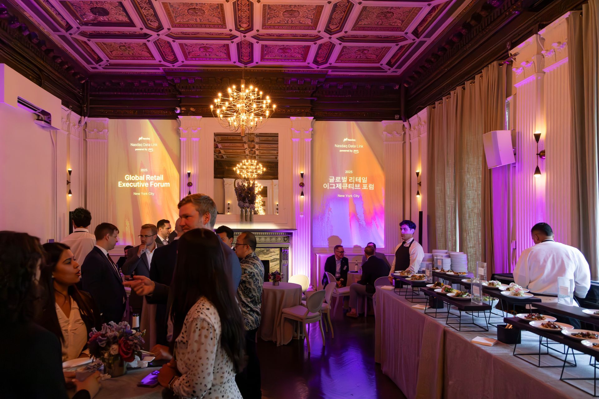 Elegant banquet hall with guests mingling under chandeliers and a buffet table along the right wall