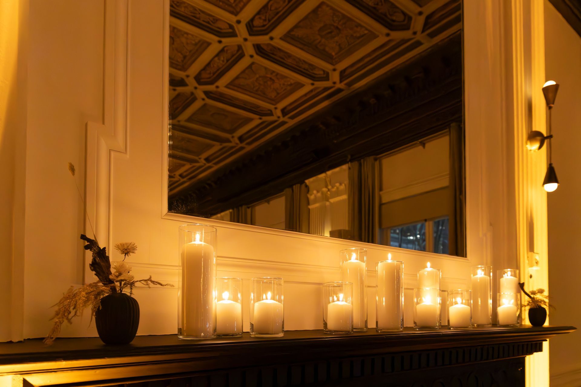 Candles glowing on a windowsill beside a vase of flowers in a warmly lit room