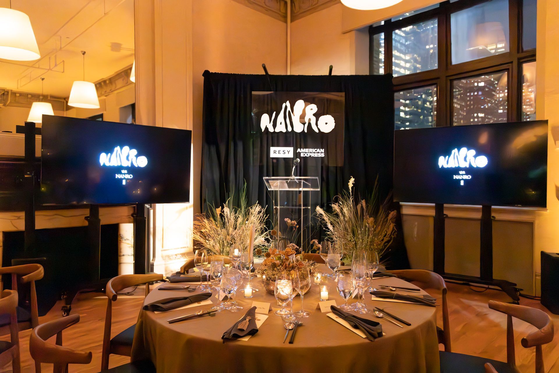 Elegant banquet table with candles and flowers, flanked by two screens in a warm-lit event hall
