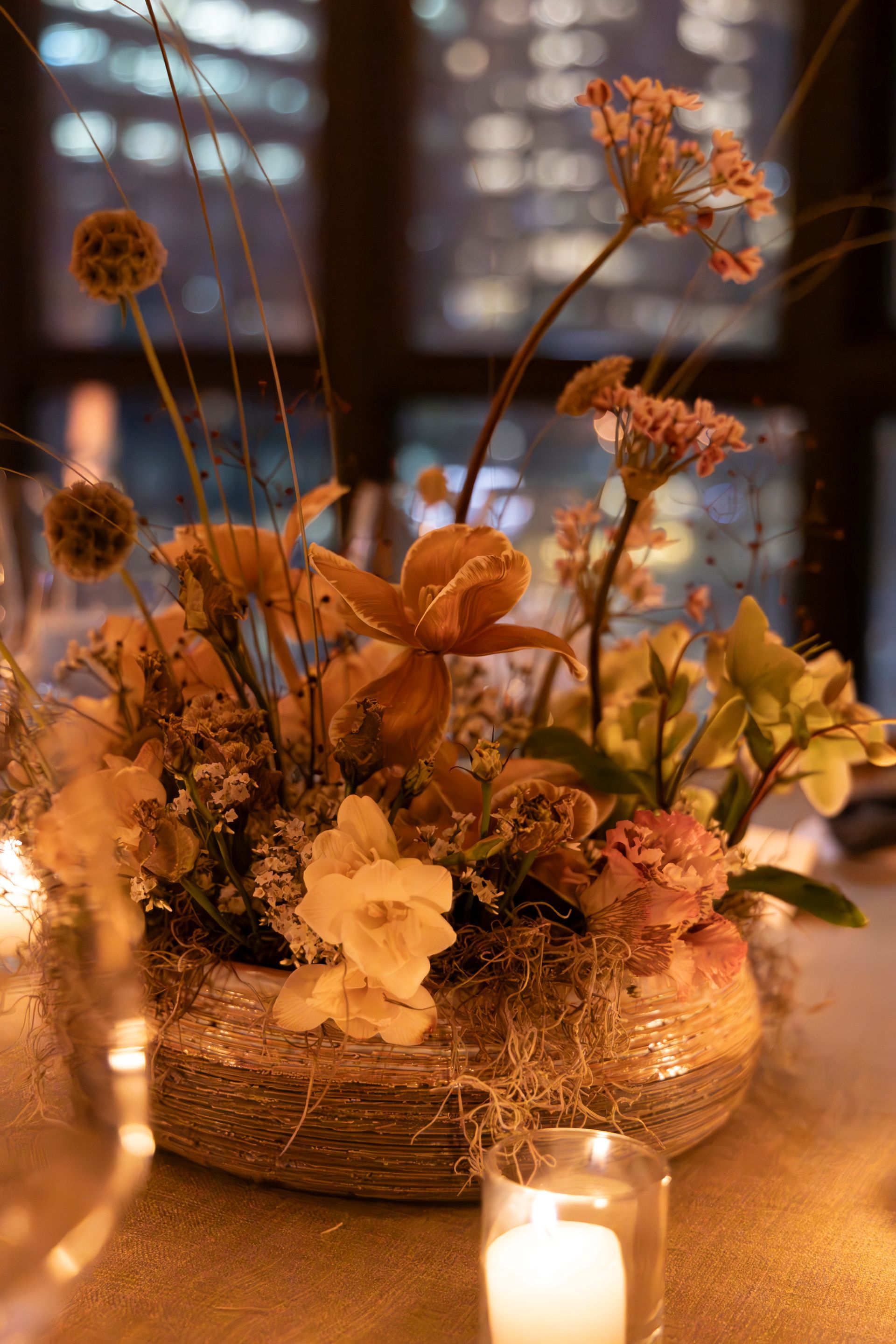 Warm candlelit floral centerpiece with dried orange and cream flowers in a woven basket on a table
