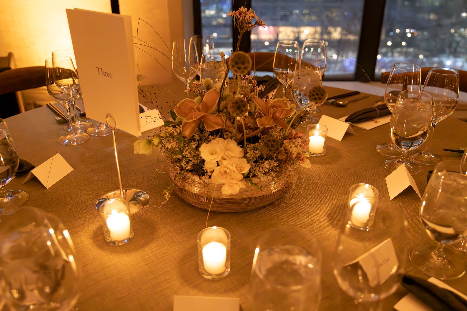 Candlelit banquet table with floral centerpiece, glassware, and folded place cards at sunset.