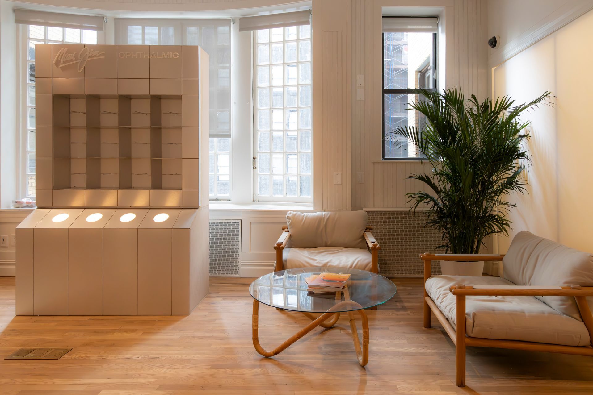 Bright living room with a wooden shelf display, sofa, glass coffee table, and tall windows.